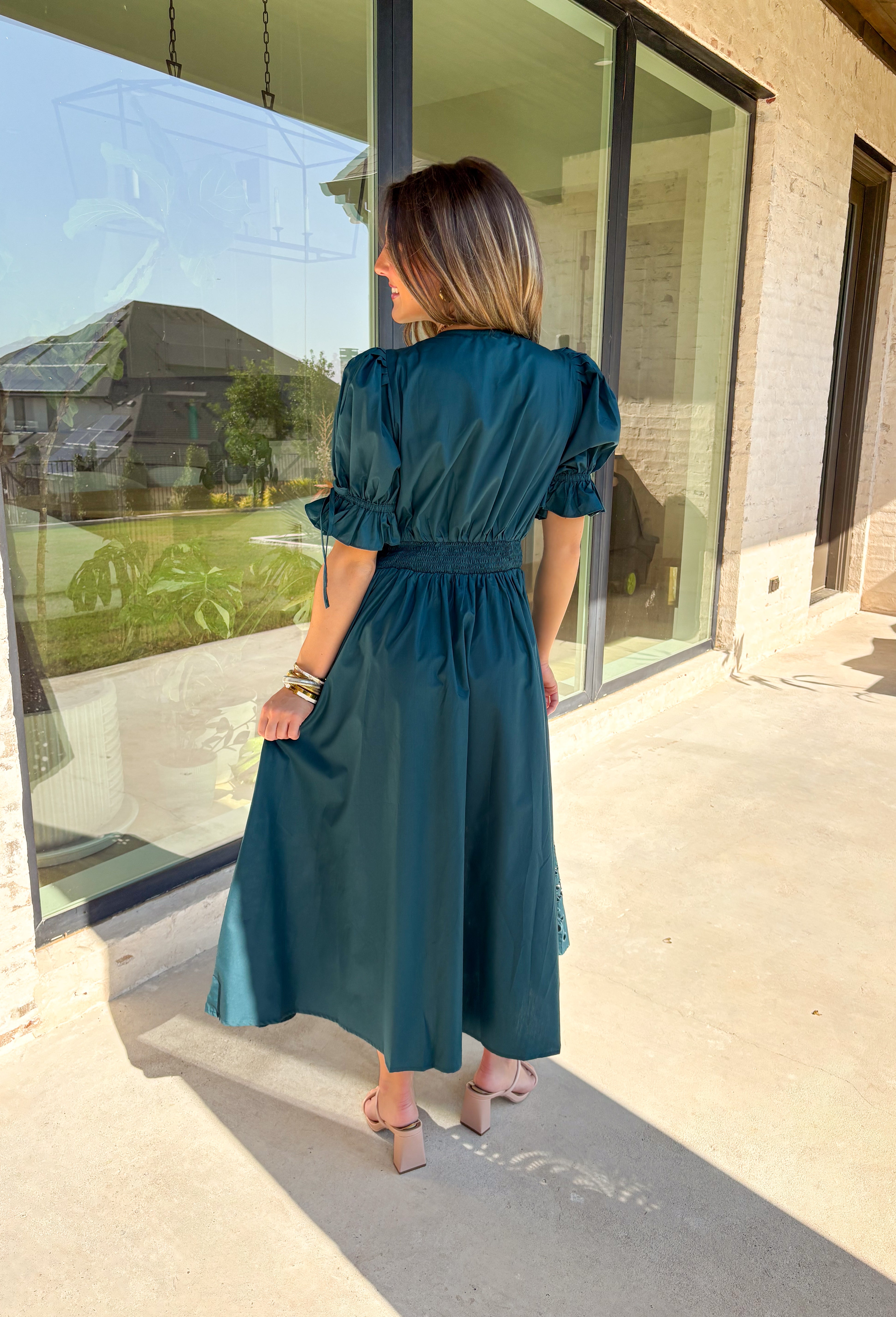 A statement piece with a touch of whimsy, this teal midi dress is designed to turn heads. Short puff sleeves and a flattering stitch-accent v-neckline pair beautifully with a defined waistband, while the embroidered skirt hem adds that extra bit of charm. The zipper front closure offers a modern twist, and the smocked waistband at the back ensures all-day comfort. This is perfect for any fall occasion!