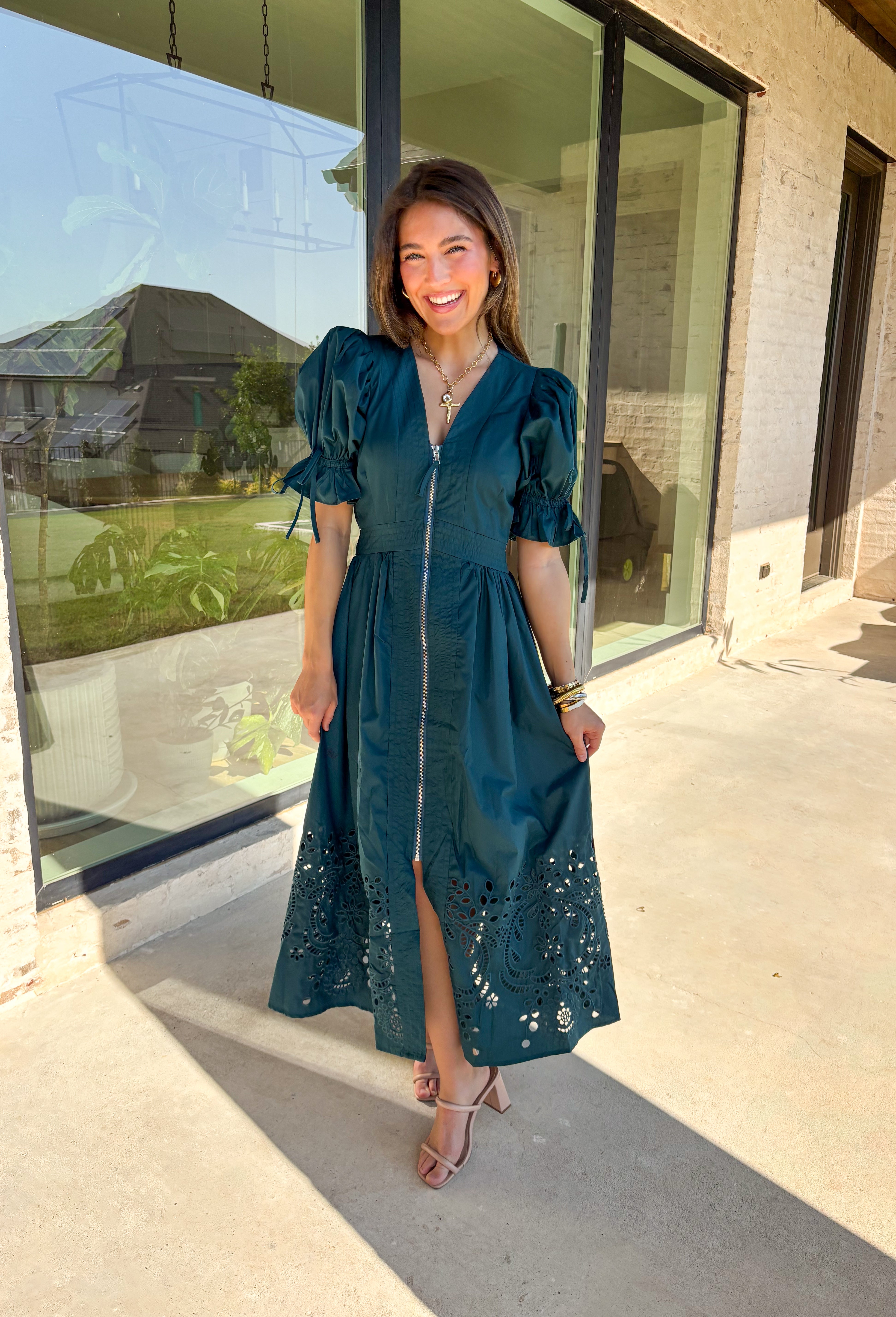 A statement piece with a touch of whimsy, this teal midi dress is designed to turn heads. Short puff sleeves and a flattering stitch-accent v-neckline pair beautifully with a defined waistband, while the embroidered skirt hem adds that extra bit of charm. The zipper front closure offers a modern twist, and the smocked waistband at the back ensures all-day comfort. This is perfect for any fall occasion!