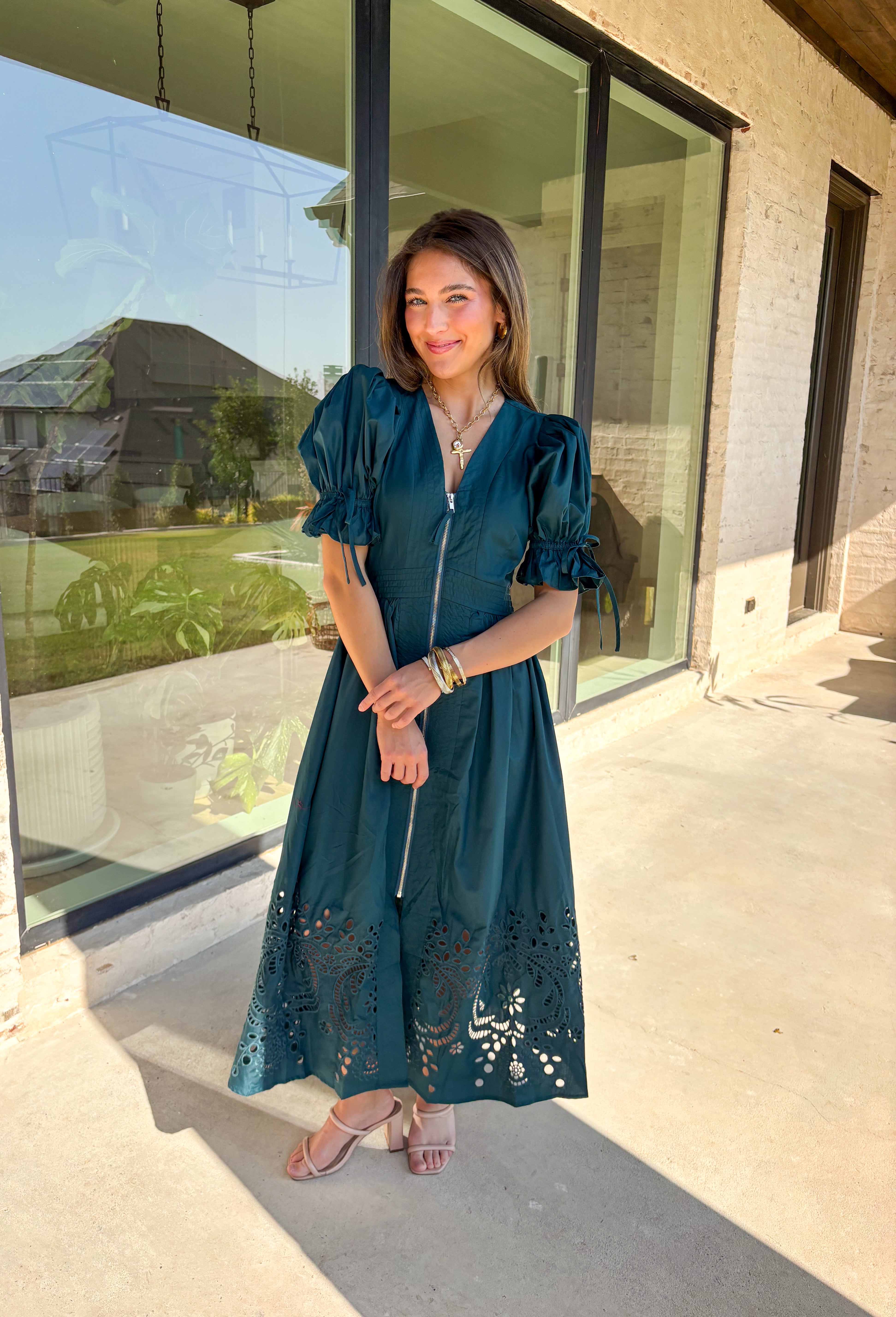 A statement piece with a touch of whimsy, this teal midi dress is designed to turn heads. Short puff sleeves and a flattering stitch-accent v-neckline pair beautifully with a defined waistband, while the embroidered skirt hem adds that extra bit of charm. The zipper front closure offers a modern twist, and the smocked waistband at the back ensures all-day comfort. This is perfect for any fall occasion!