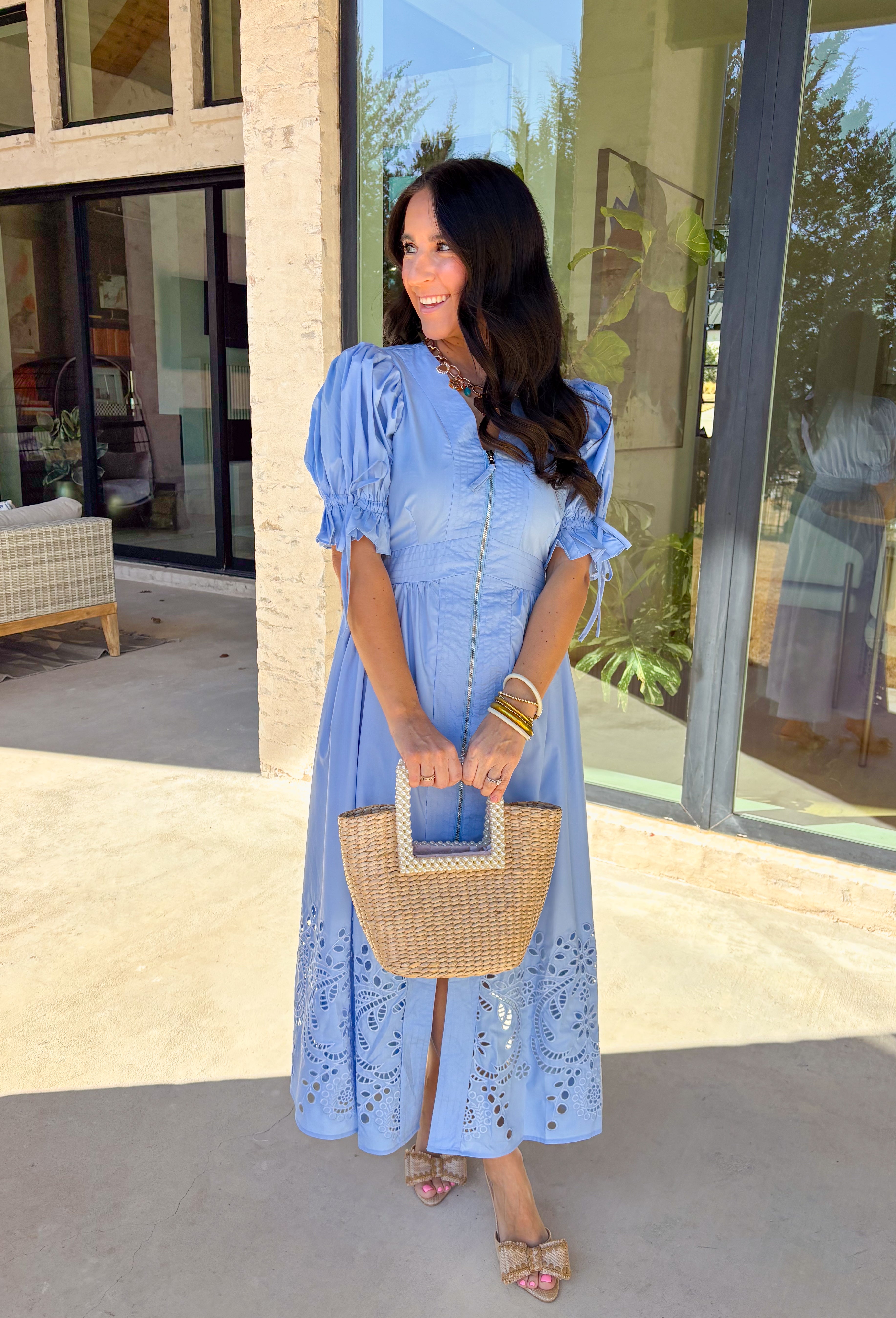 A statement piece with a touch of whimsy, this light blue midi dress is designed to turn heads. Short puff sleeves and a flattering stitch-accent v-neckline pair beautifully with a defined waistband, while the embroidered skirt hem adds that extra bit of charm. The zipper front closure offers a modern twist, and the smocked waistband at the back ensures all-day comfort. This is perfect for any spring occasion!
