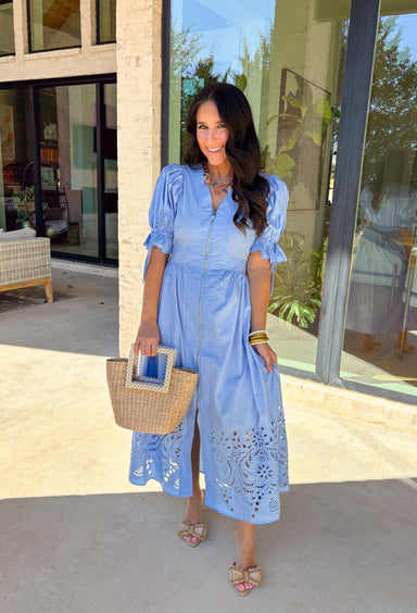 A statement piece with a touch of whimsy, this light blue midi dress is designed to turn heads. Short puff sleeves and a flattering stitch-accent v-neckline pair beautifully with a defined waistband, while the embroidered skirt hem adds that extra bit of charm. The zipper front closure offers a modern twist, and the smocked waistband at the back ensures all-day comfort. This is perfect for any spring occasion!