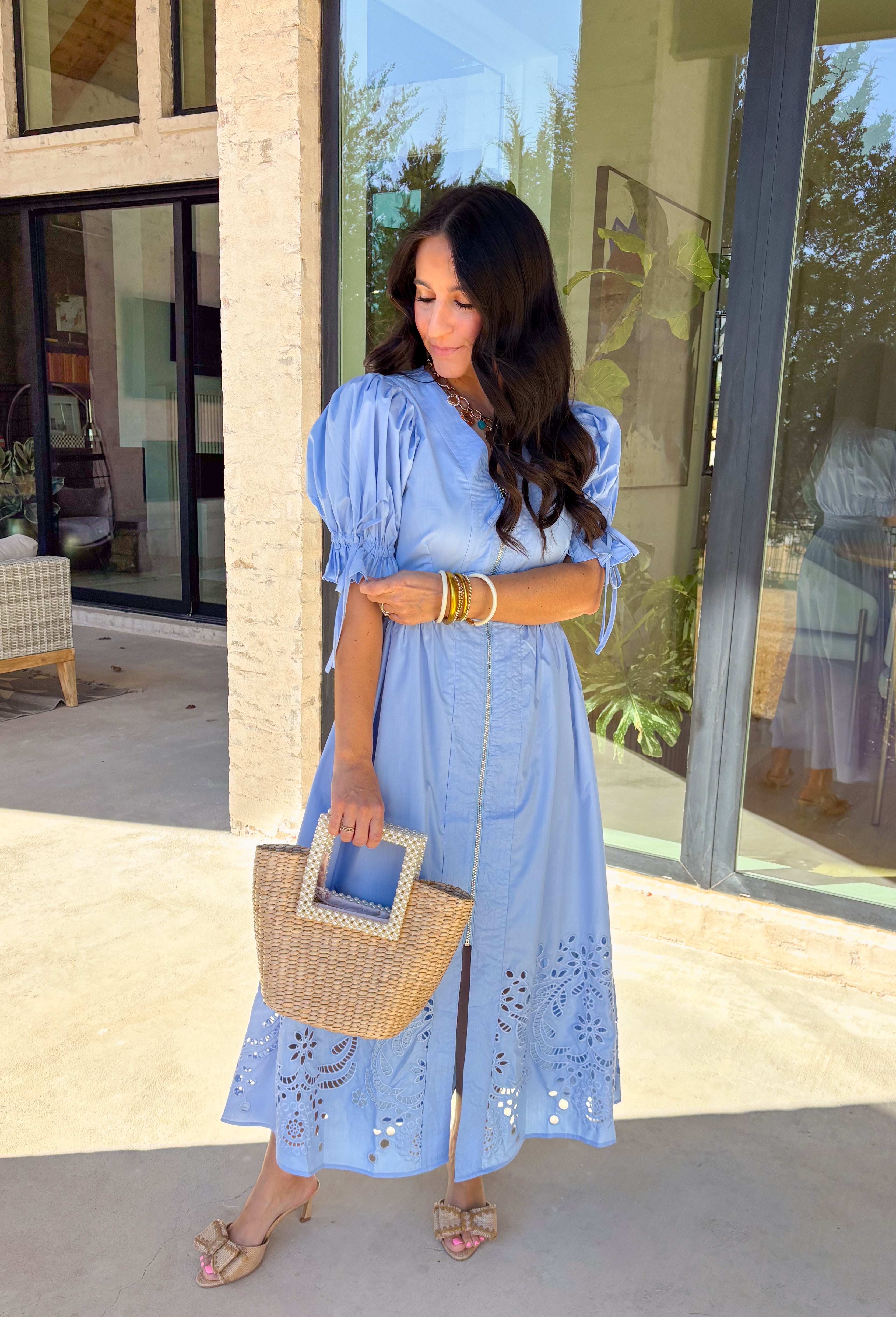 A statement piece with a touch of whimsy, this light blue midi dress is designed to turn heads. Short puff sleeves and a flattering stitch-accent v-neckline pair beautifully with a defined waistband, while the embroidered skirt hem adds that extra bit of charm. The zipper front closure offers a modern twist, and the smocked waistband at the back ensures all-day comfort. This is perfect for any spring occasion!