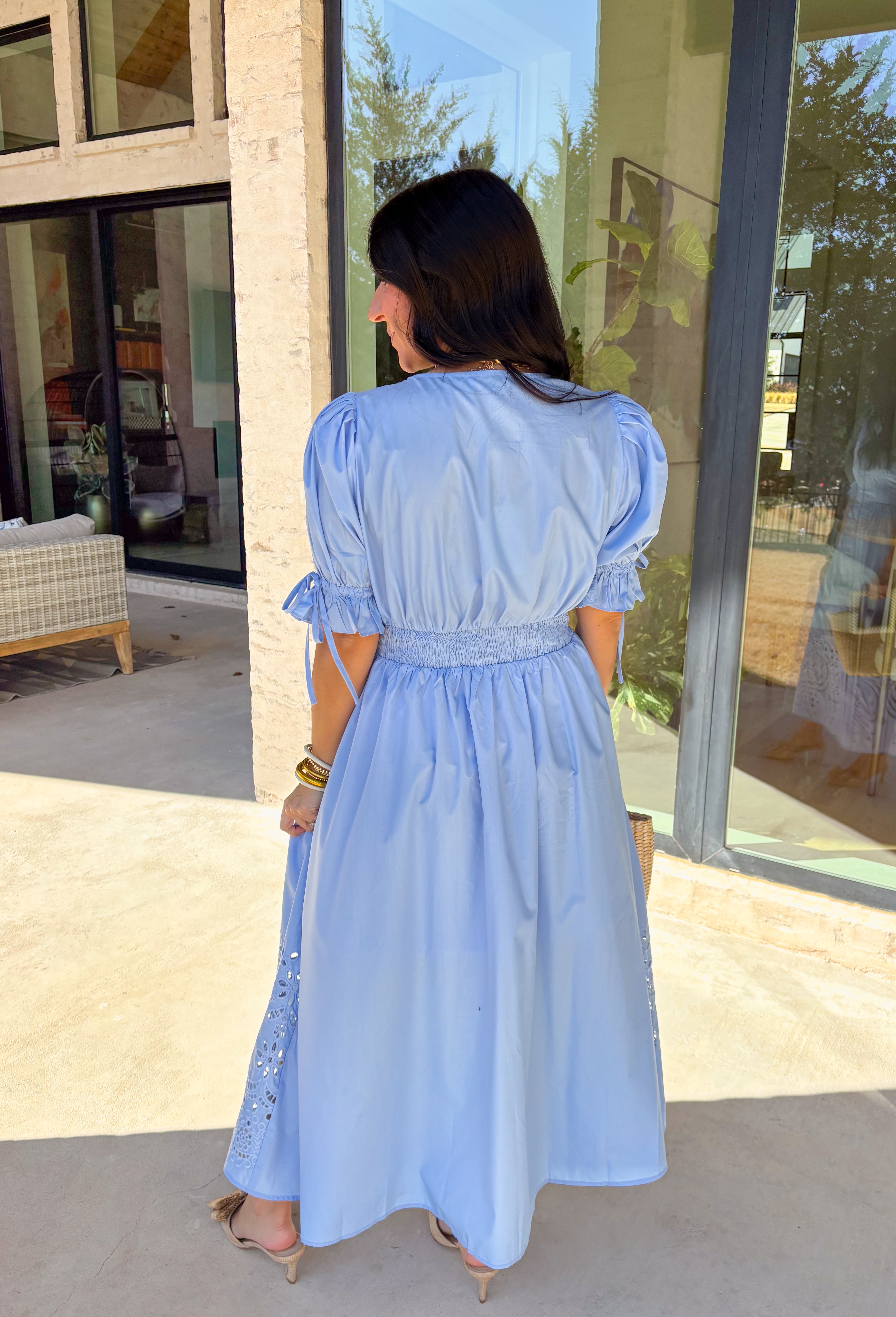 A statement piece with a touch of whimsy, this light blue midi dress is designed to turn heads. Short puff sleeves and a flattering stitch-accent v-neckline pair beautifully with a defined waistband, while the embroidered skirt hem adds that extra bit of charm. The zipper front closure offers a modern twist, and the smocked waistband at the back ensures all-day comfort. This is perfect for any spring occasion!
