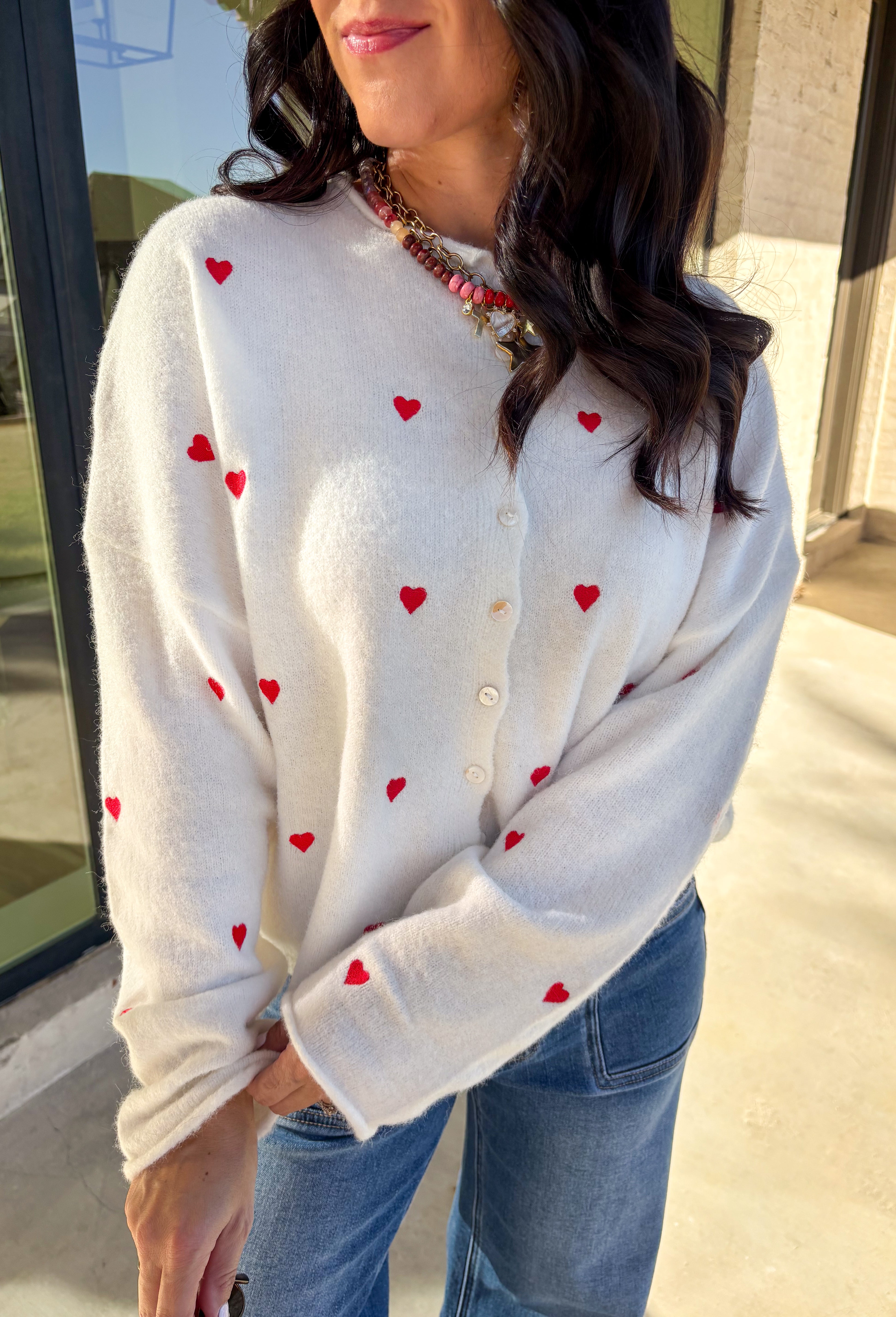 Add a little love to your look with this darling white button-down cardigan by Things Between. Featuring red embroidered hearts throughout and a scalloped trim along the front, this cozy knit is the perfect mix of cute and classic. Soft, feminine, and full of charm, it’s the perfect layer for Valentine’s Day and beyond.
