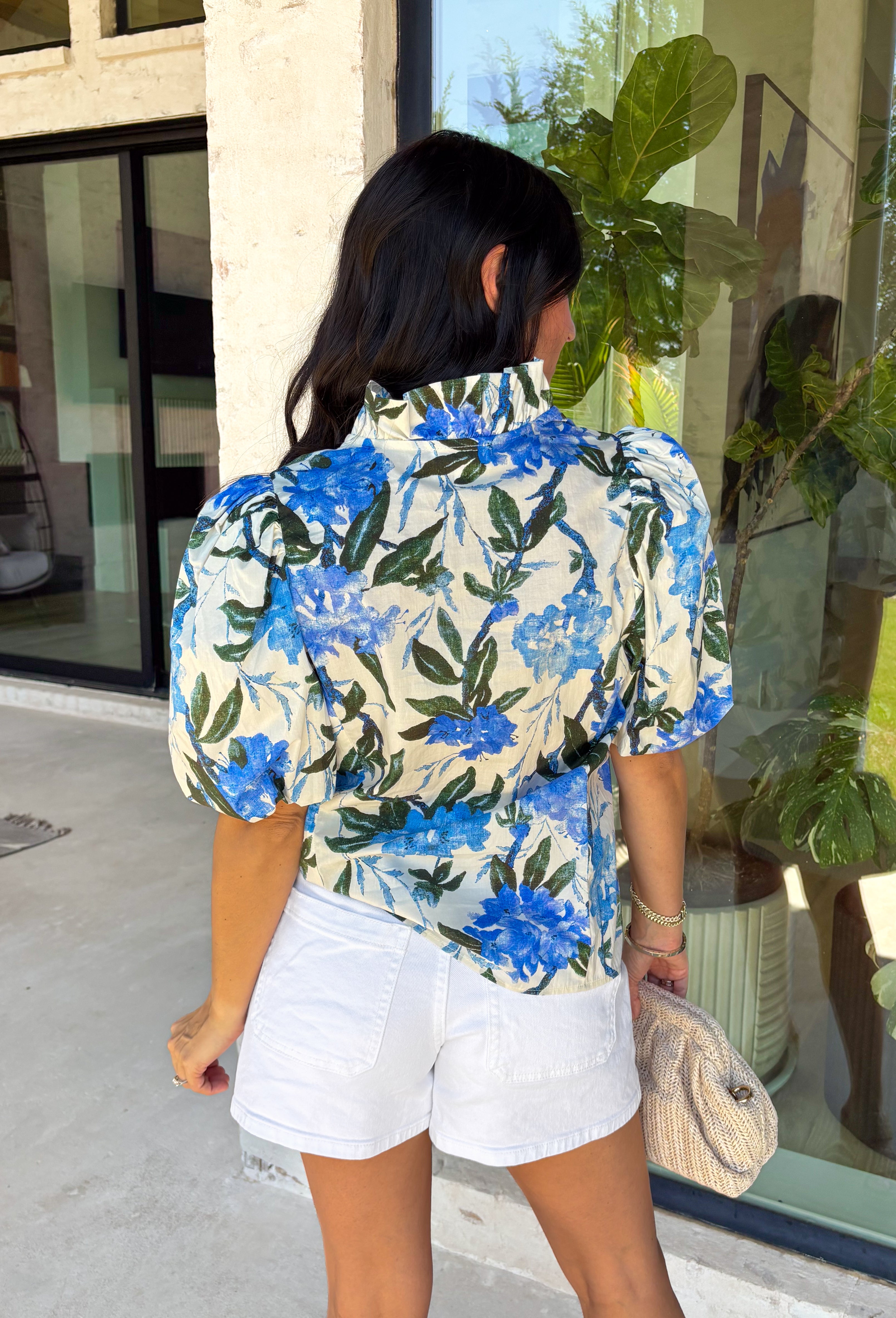 Fresh, feminine, and perfect for spring, this off-white button-down top by Entro is an easy standout. Featuring a blue floral print with pops of hunter green, it gives you the prettiest mix of color while still feeling classic and wearable. The ruffle neckline adds a sweet, polished touch, and puff sleeves bring that soft, feminine silhouette we love. Made from breathable cotton, this top is perfect for sunny days, brunch plans, and effortless spring outfits.