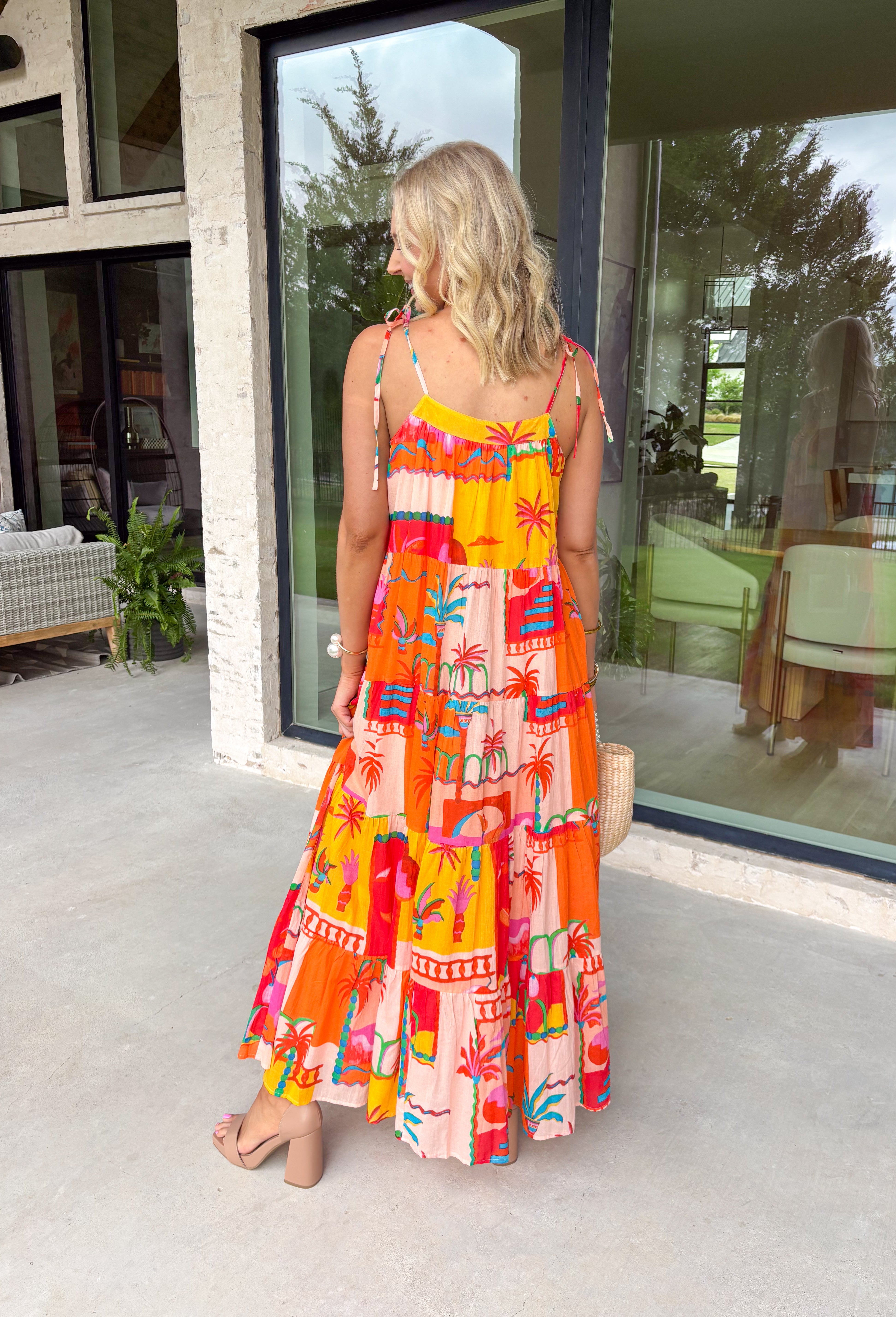 This orange sleeveless midi dress is pure sunshine in outfit form. Covered in a vibrant tropical print with pops of yellow, blue, green, and red, it instantly brings bold, vacation-ready energy to your wardrobe. The adjustable tie straps add a sweet, feminine touch while allowing for a customizable fit. Designed with a flowy tiered skirt and fully lined for easy wear, this dress is made for warm days, beach getaways, and sunny celebrations.