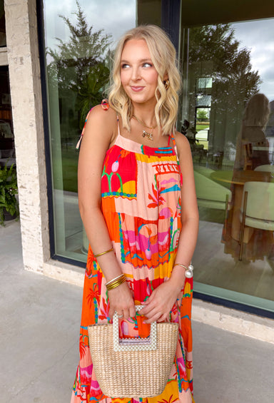 This orange sleeveless midi dress is pure sunshine in outfit form. Covered in a vibrant tropical print with pops of yellow, blue, green, and red, it instantly brings bold, vacation-ready energy to your wardrobe. The adjustable tie straps add a sweet, feminine touch while allowing for a customizable fit. Designed with a flowy tiered skirt and fully lined for easy wear, this dress is made for warm days, beach getaways, and sunny celebrations.