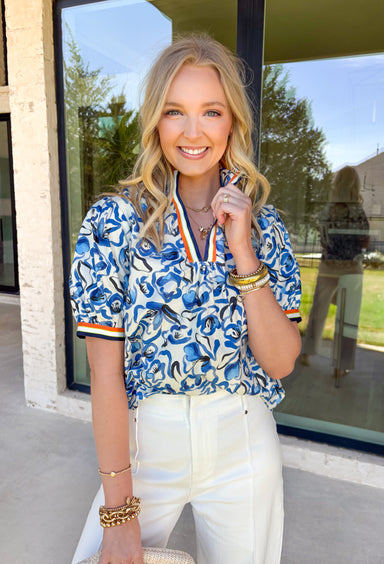 This short sleeve top by Voy is such a fun, fresh piece for spring! With its blue and white abstract floral print, it feels light, cheerful, and easy to style for everyday wear. The contrast trim along the neckline and sleeve cuffs adds the perfect pop of color in navy, white, green, and orange—giving it that extra little “wow” detail that makes it stand out from a basic top. Made from 100% cotton, it’s breathable and comfy for warm days, and it pairs effortlessly with everything.