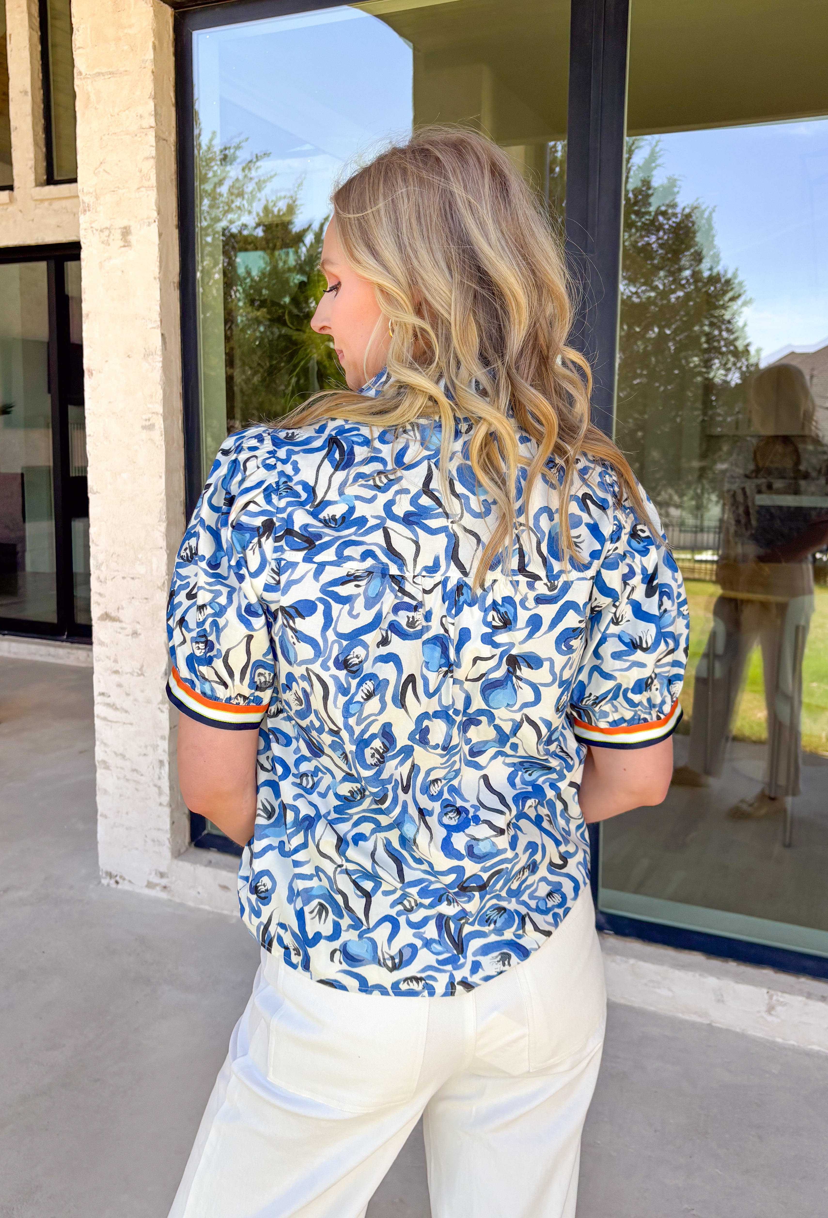 This short sleeve top by Voy is such a fun, fresh piece for spring! With its blue and white abstract floral print, it feels light, cheerful, and easy to style for everyday wear. The contrast trim along the neckline and sleeve cuffs adds the perfect pop of color in navy, white, green, and orange—giving it that extra little “wow” detail that makes it stand out from a basic top. Made from 100% cotton, it’s breathable and comfy for warm days, and it pairs effortlessly with everything.