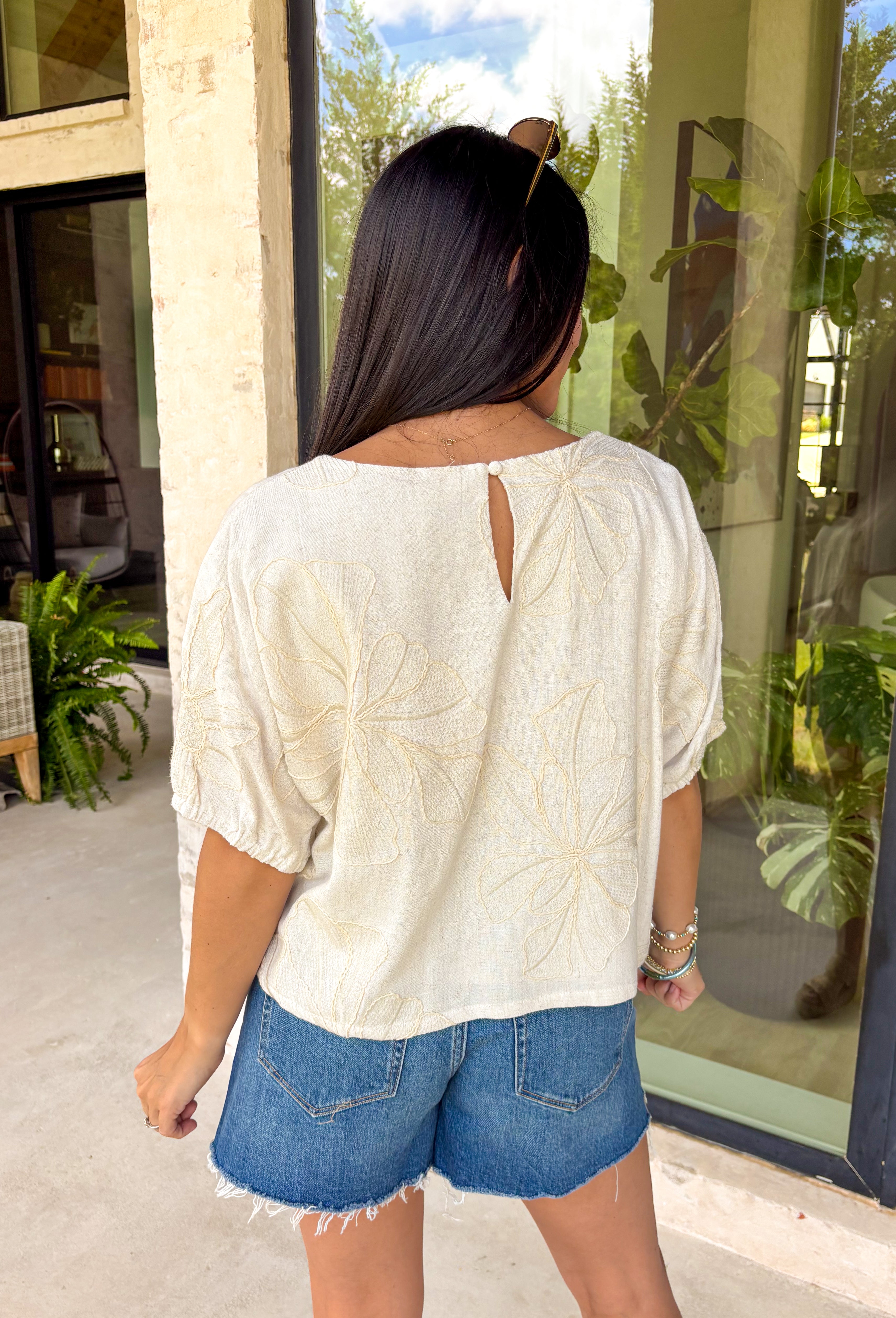 Understated and effortlessly pretty, this khaki short sleeve top is all about the details. The monochromatic floral embroidery adds soft texture without overwhelming the look, giving it that elevated, timeless feel you’ll reach for again and again. Designed with elastic cuff sleeves for a subtle puff effect and finished with a delicate keyhole closure in the back, this top blends feminine touches with everyday ease. The breathable linen blend keeps it lightweight and comfortable.