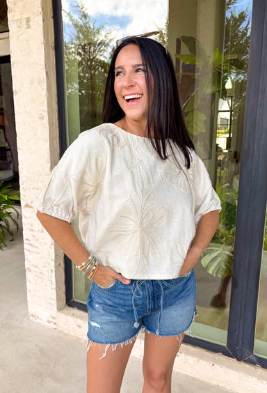 Understated and effortlessly pretty, this khaki short sleeve top is all about the details. The monochromatic floral embroidery adds soft texture without overwhelming the look, giving it that elevated, timeless feel you’ll reach for again and again. Designed with elastic cuff sleeves for a subtle puff effect and finished with a delicate keyhole closure in the back, this top blends feminine touches with everyday ease. The breathable linen blend keeps it lightweight and comfortable.