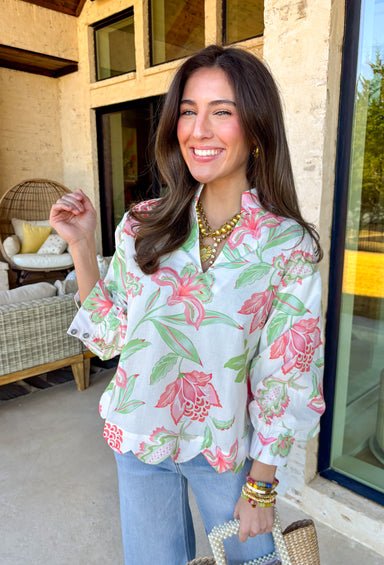 Fresh, colorful, and effortlessly pretty, this white long sleeve top by Entro is a perfect spring staple. Featuring a cheerful floral print in coral and green, it adds a bright pop of color while still feeling light and wearable. The v-neck band collar gives it a clean, polished look, while the scalloped hem adds a sweet, feminine finish. Buttoned cuffs complete the look, making this top easy to dress up or wear casually all season long.