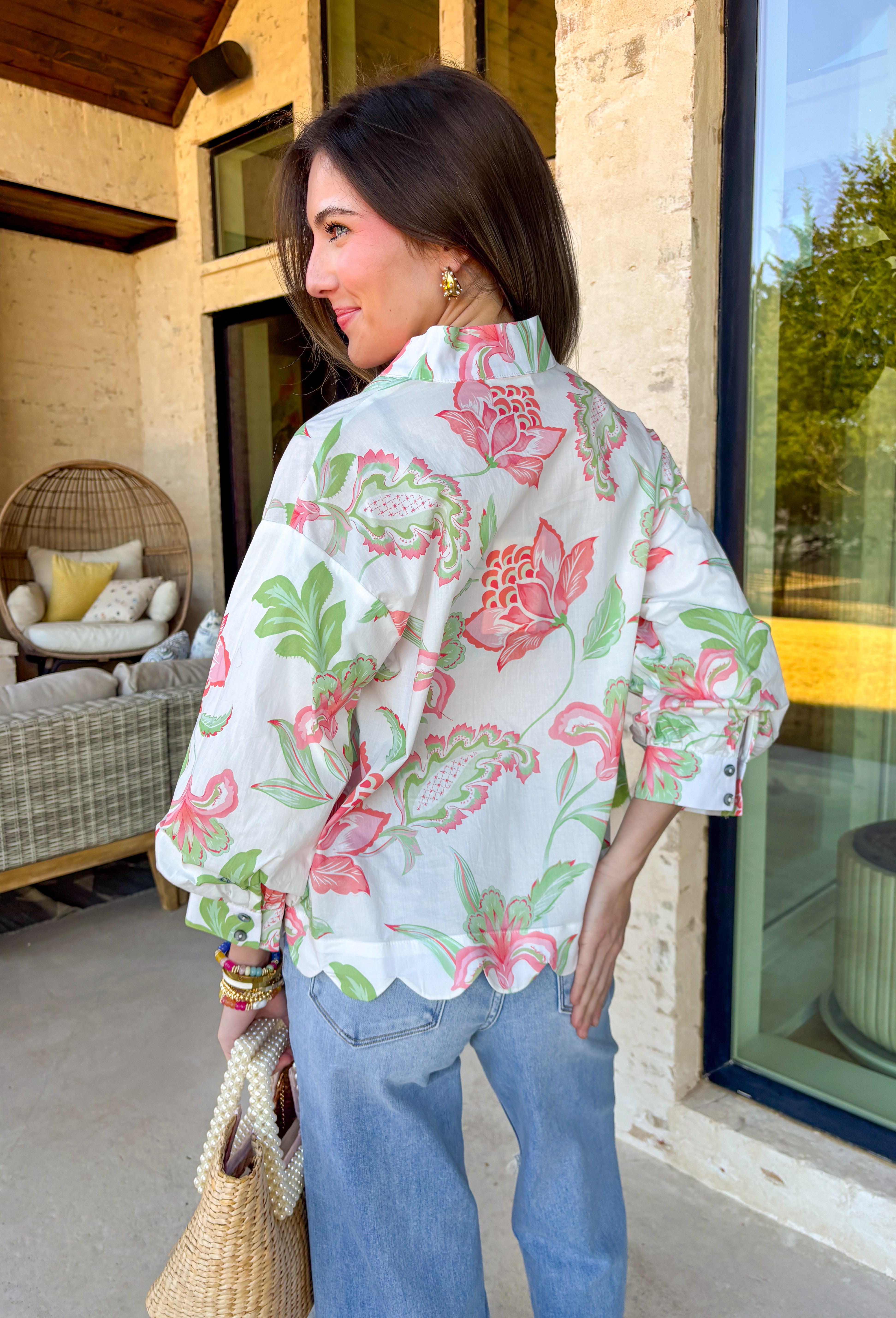 Fresh, colorful, and effortlessly pretty, this white long sleeve top by Entro is a perfect spring staple. Featuring a cheerful floral print in coral and green, it adds a bright pop of color while still feeling light and wearable. The v-neck band collar gives it a clean, polished look, while the scalloped hem adds a sweet, feminine finish. Buttoned cuffs complete the look, making this top easy to dress up or wear casually all season long.