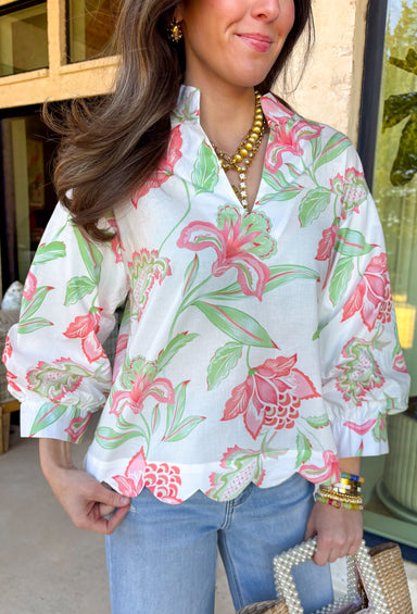 Fresh, colorful, and effortlessly pretty, this white long sleeve top by Entro is a perfect spring staple. Featuring a cheerful floral print in coral and green, it adds a bright pop of color while still feeling light and wearable. The v-neck band collar gives it a clean, polished look, while the scalloped hem adds a sweet, feminine finish. Buttoned cuffs complete the look, making this top easy to dress up or wear casually all season long.