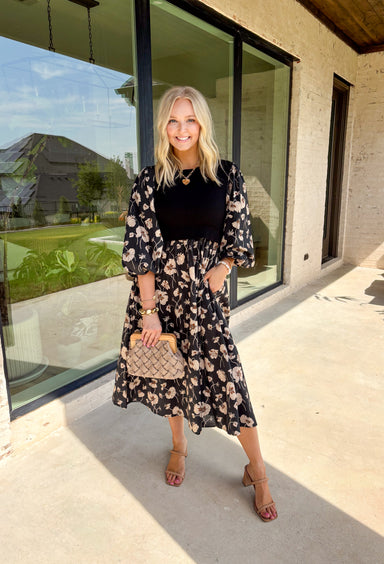All the layered style, none of the layering fuss—this black midi dress makes autumn dressing a breeze. With a soft neutral floral print and solid black ribbed front panel, it creates that effortless "sweater over dress" vibe without adding bulk. The balloon sleeves and elastic cuffs give it a romantic, flowy feel, while the midi length keeps it versatile for boots or flats. Comfortable, polished, and totally ready for cooler days, this dress is the perfect blend of cozy and put-together.