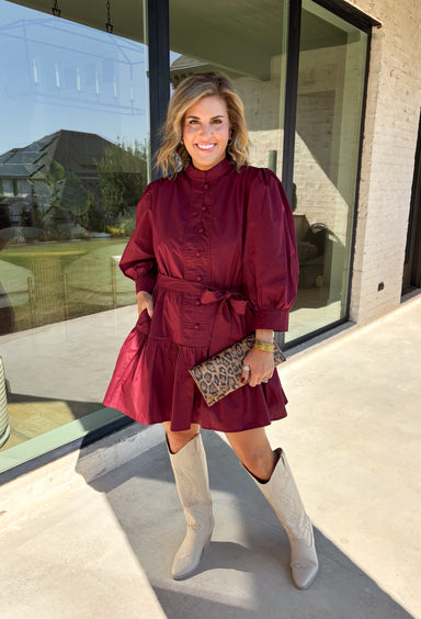 Rich burgundy makes this dress from Entro an easy favorite for all the plans filling up your fall calendar. The stand collar and split neckline create a classic look, while the button-front closure adds a pretty finishing detail. Long balloon sleeves bring soft volume to the silhouette and are finished with button cuffs for a more tailored touch. A removable self-tie belt lets you define the waist or switch up the look, while the tiered skirt adds movement and shape. 