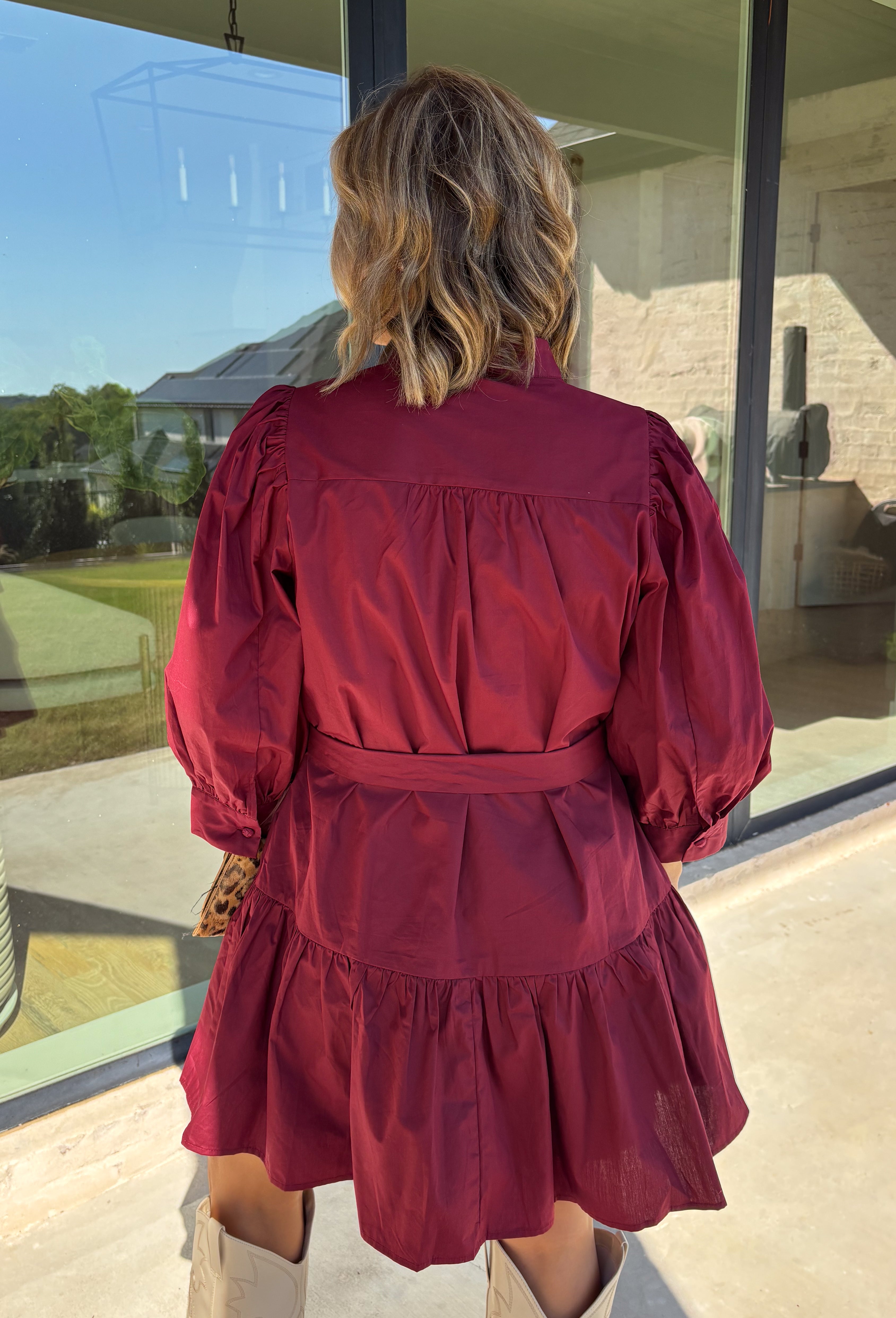 Rich burgundy makes this dress from Entro an easy favorite for all the plans filling up your fall calendar. The stand collar and split neckline create a classic look, while the button-front closure adds a pretty finishing detail. Long balloon sleeves bring soft volume to the silhouette and are finished with button cuffs for a more tailored touch. A removable self-tie belt lets you define the waist or switch up the look, while the tiered skirt adds movement and shape. 