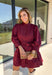 Rich burgundy makes this dress from Entro an easy favorite for all the plans filling up your fall calendar. The stand collar and split neckline create a classic look, while the button-front closure adds a pretty finishing detail. Long balloon sleeves bring soft volume to the silhouette and are finished with button cuffs for a more tailored touch. A removable self-tie belt lets you define the waist or switch up the look, while the tiered skirt adds movement and shape. 
