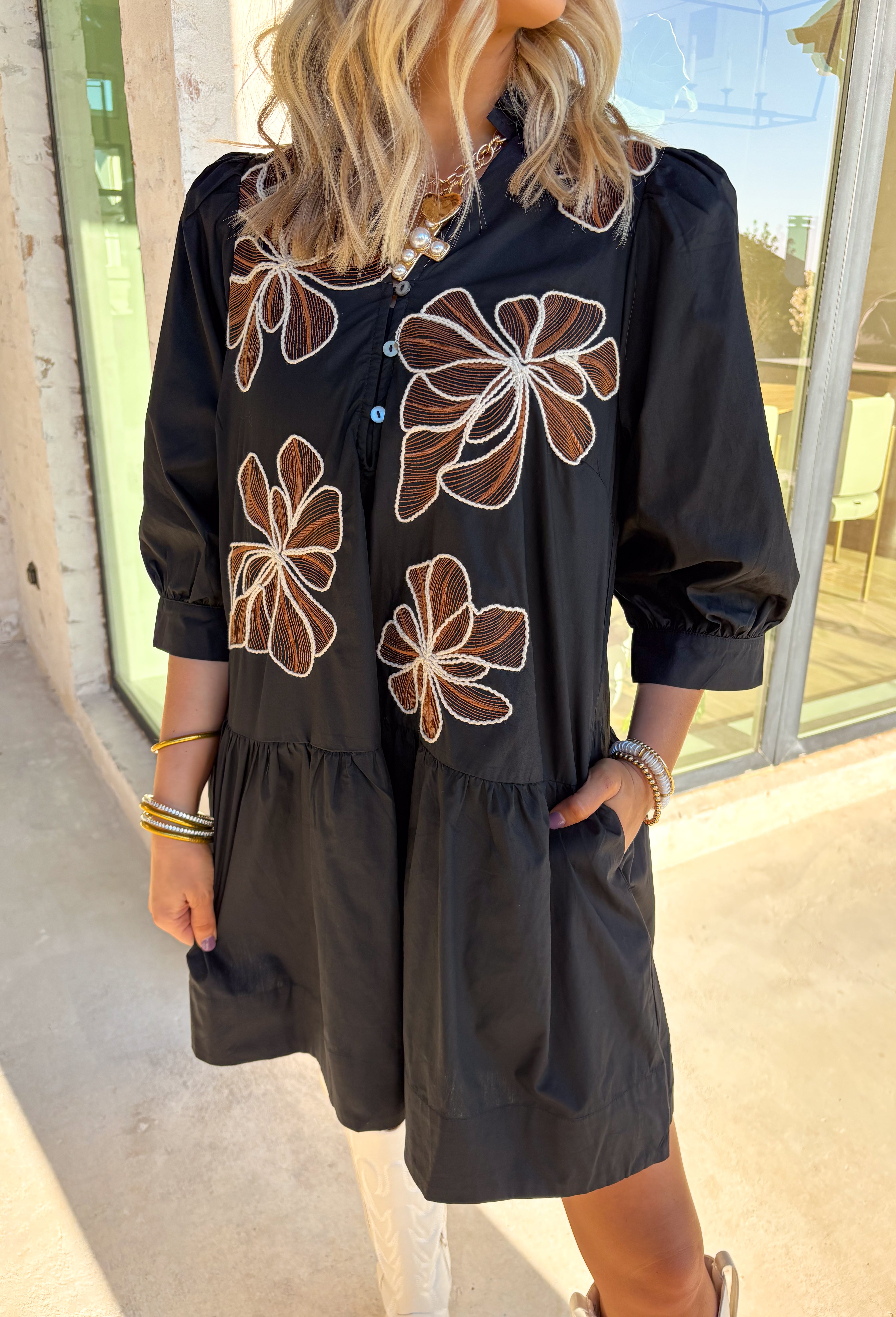 Elegant with a touch of autumn charm, this black dress by Entro features intricate rust and off-white floral embroidery that makes it stand out effortlessly. The ruffled band collar and v-neckline create a soft, flattering shape, while the partial button front and ¾ sleeves keep the look timeless. Side pockets add practicality, and the full lining ensures a comfortable fit. A perfect pick for everything from brunch to special fall occasions.