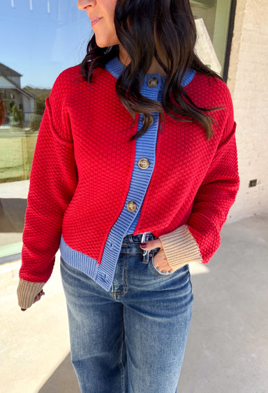 A cozy layering essential with a playful twist! This red knit button down cardigan features hints of periwinkle woven throughout for a fun pop of color, plus a contrasting tan trim on the sleeves for that little something extra. It’s the kind of cardigan you’ll reach for all season long—whether you're lounging or layering up for fall errands.