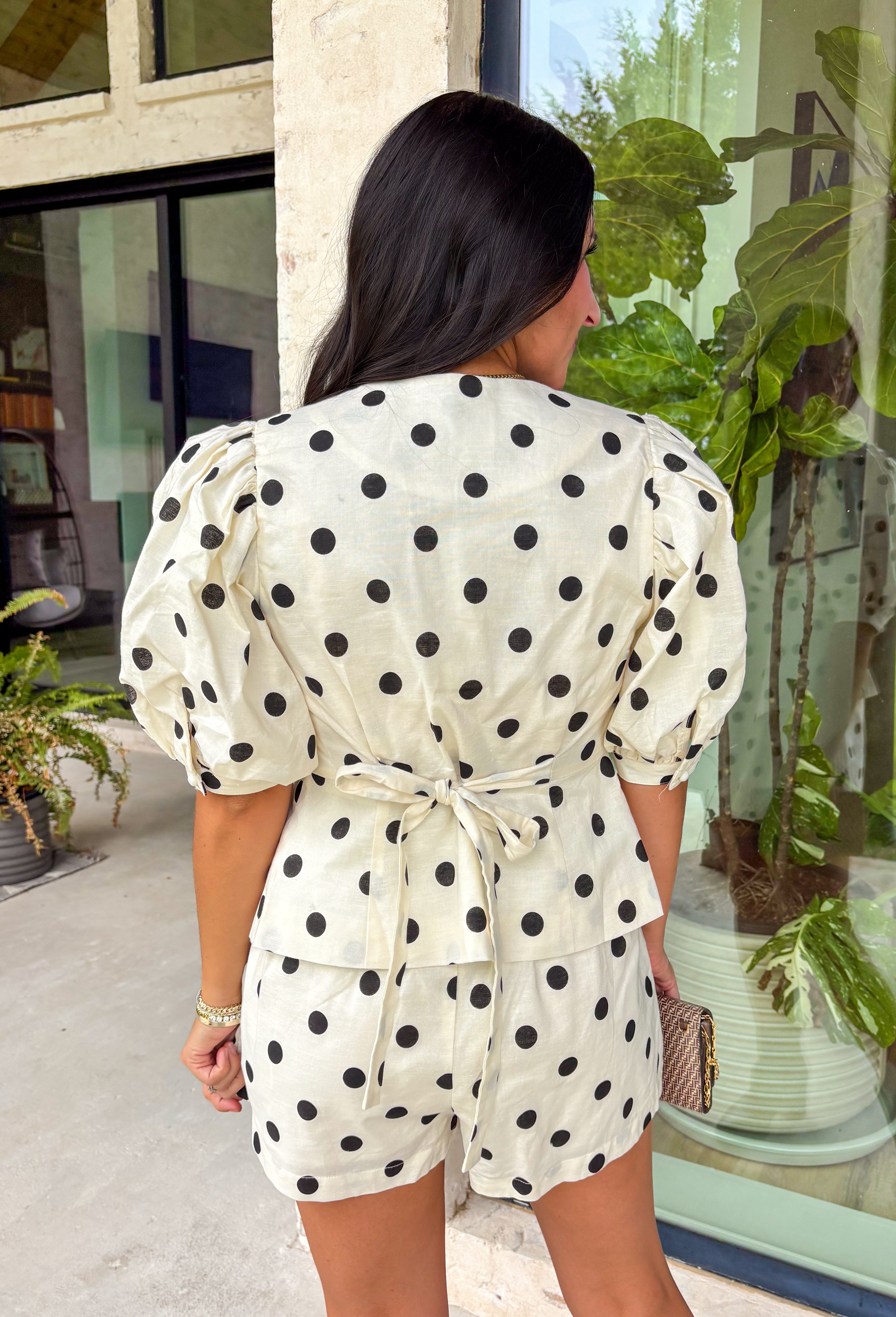 Classic polka dots and effortless style come together in this adorable two-piece set from Mable. Featuring an off-white and black polka dot print, this coordinating outfit is as versatile as it is charming. The short sleeve top is designed with feminine puff sleeves, a single button closure at the front, and a sweet tie detail at the back for an elevated finish. The matching shorts feature a comfortable elastic waistband, side zipper closure, and functional side pockets.