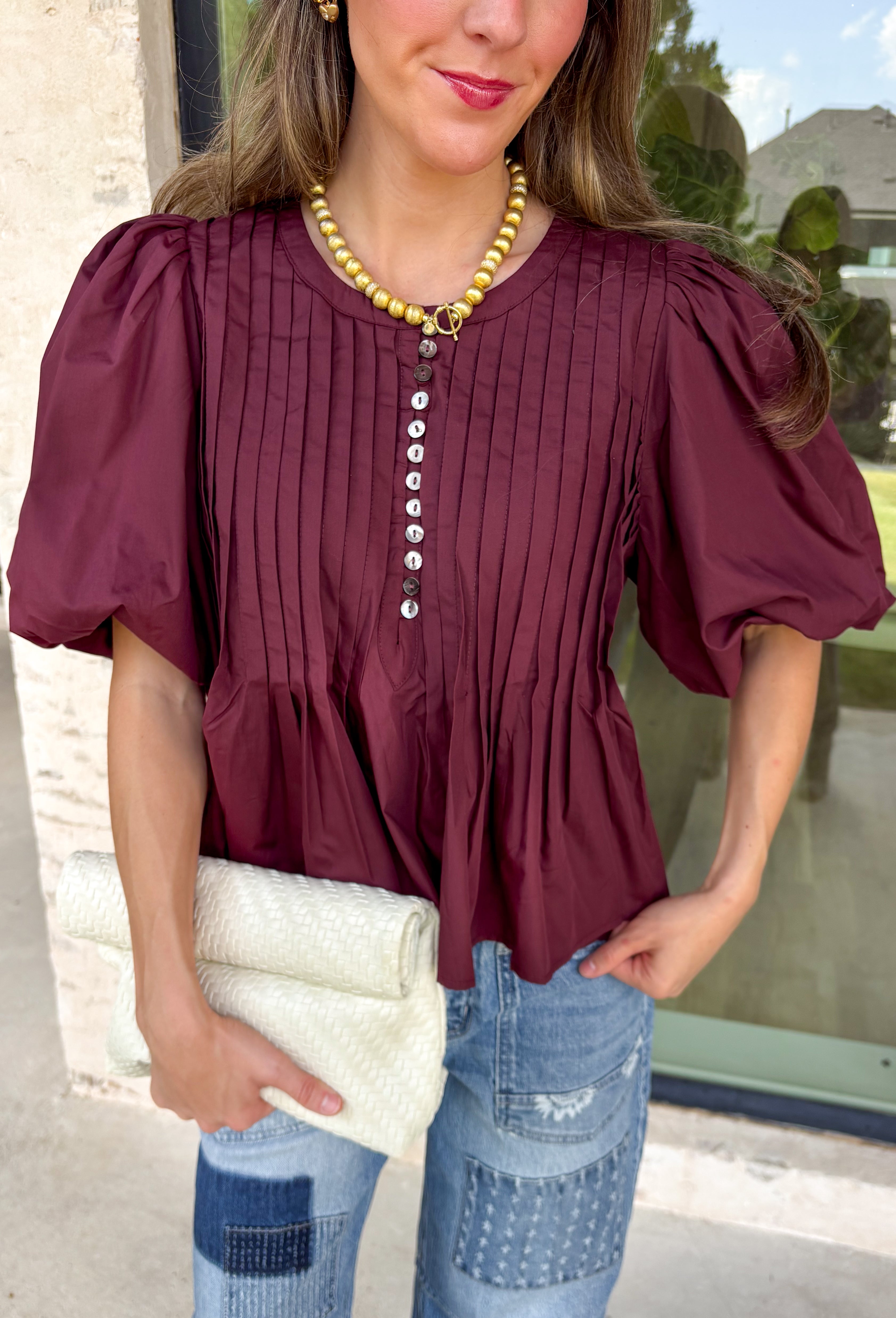 Elevate your everyday wardrobe with this beautifully detailed top from Entro. Designed in a rich merlot hue, this timeless blouse features elegant pleating throughout for added texture and a polished finish. Decorative front button details add classic charm, while the puff sleeves create a feminine silhouette that's easy to dress up or down. Crafted from a lightweight fabric blend, this versatile top is perfect for everything from workdays to weekend brunches and seasonal gatherings.