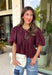Elevate your everyday wardrobe with this beautifully detailed top from Entro. Designed in a rich merlot hue, this timeless blouse features elegant pleating throughout for added texture and a polished finish. Decorative front button details add classic charm, while the puff sleeves create a feminine silhouette that's easy to dress up or down. Crafted from a lightweight fabric blend, this versatile top is perfect for everything from workdays to weekend brunches and seasonal gatherings.