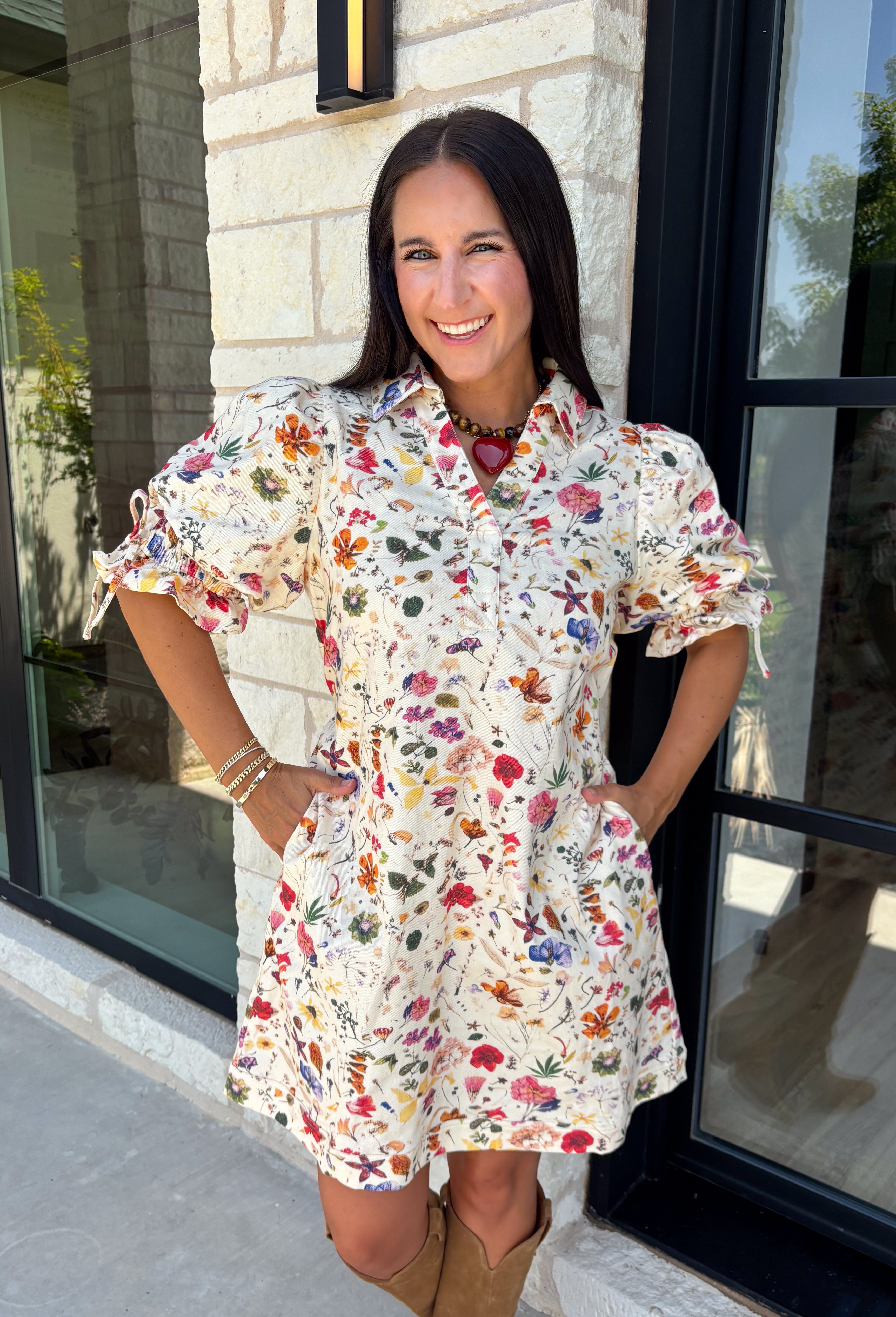 Bring a touch of color to your fall wardrobe with this effortlessly charming botanical dress. Featuring a neutral backdrop with a vibrant floral print, this feminine dress is perfect for everything from brunch dates to fall festivals. The adjustable drawstring waist creates a flattering silhouette, while the collared v-neckline and partial button placket add a timeless touch. Finished with sweet tie details at the sleeves, side pockets, and a fully lined design.