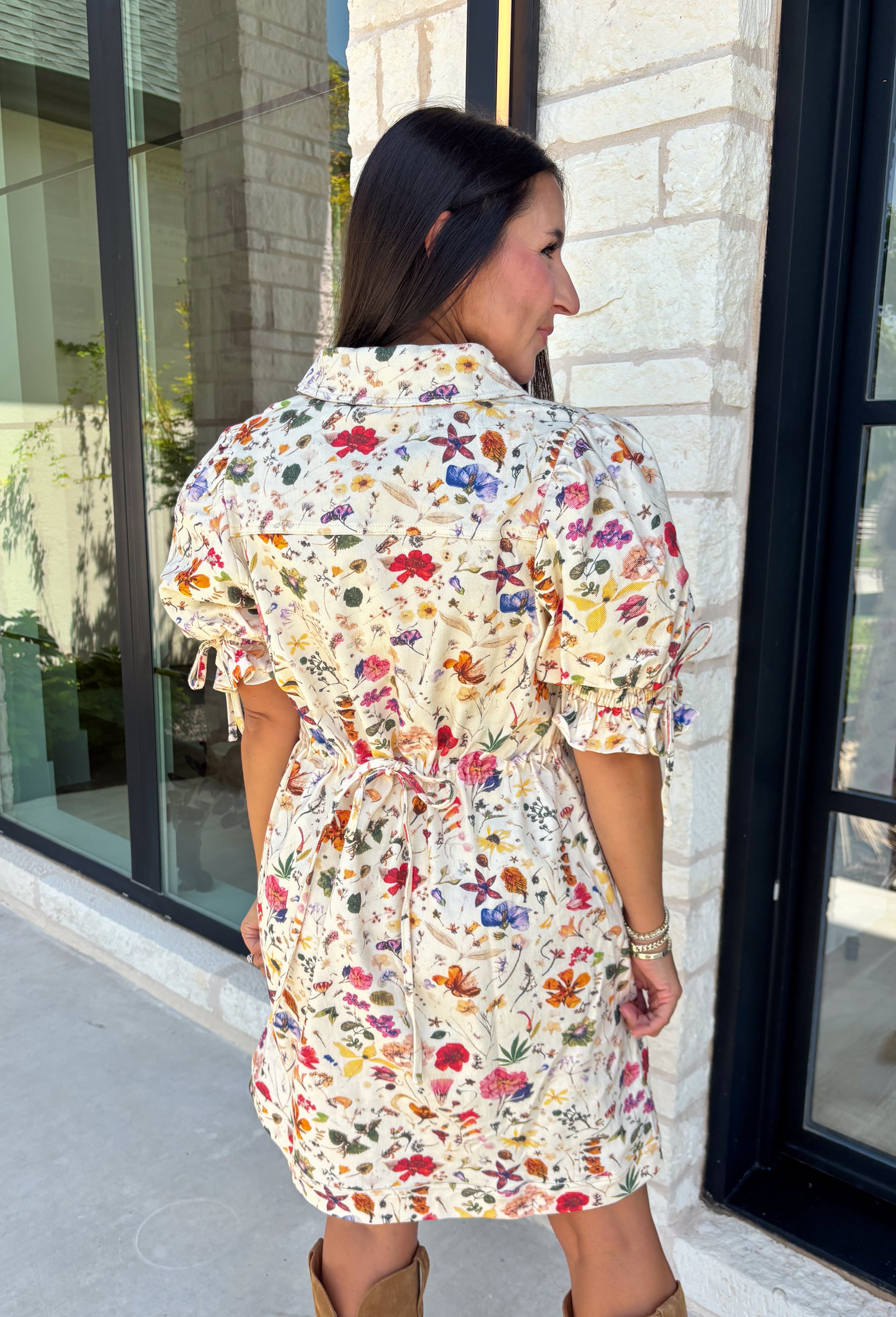 Bring a touch of color to your fall wardrobe with this effortlessly charming botanical dress. Featuring a neutral backdrop with a vibrant floral print, this feminine dress is perfect for everything from brunch dates to fall festivals. The adjustable drawstring waist creates a flattering silhouette, while the collared v-neckline and partial button placket add a timeless touch. Finished with sweet tie details at the sleeves, side pockets, and a fully lined design.