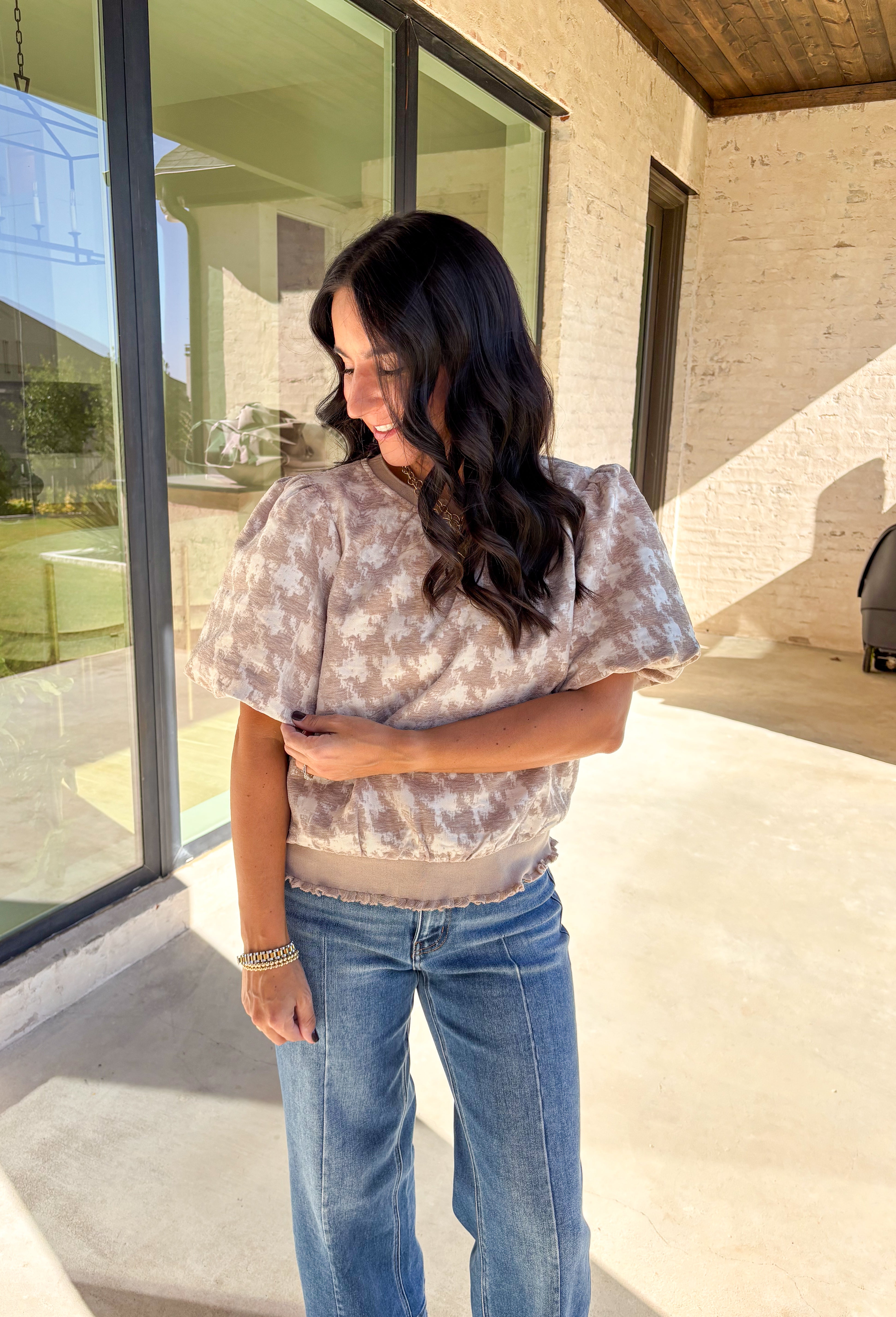 This taupe short sleeve top by Voy gives a modern twist to a timeless print. Designed with a textured abstract houndstooth pattern, it’s the perfect mix of classic and contemporary. The puff sleeves add a soft, feminine touch, while the lettuce hem brings a subtle edge to the silhouette. Lightweight and comfortable, this top easily transitions from weekday wear to special occasions.