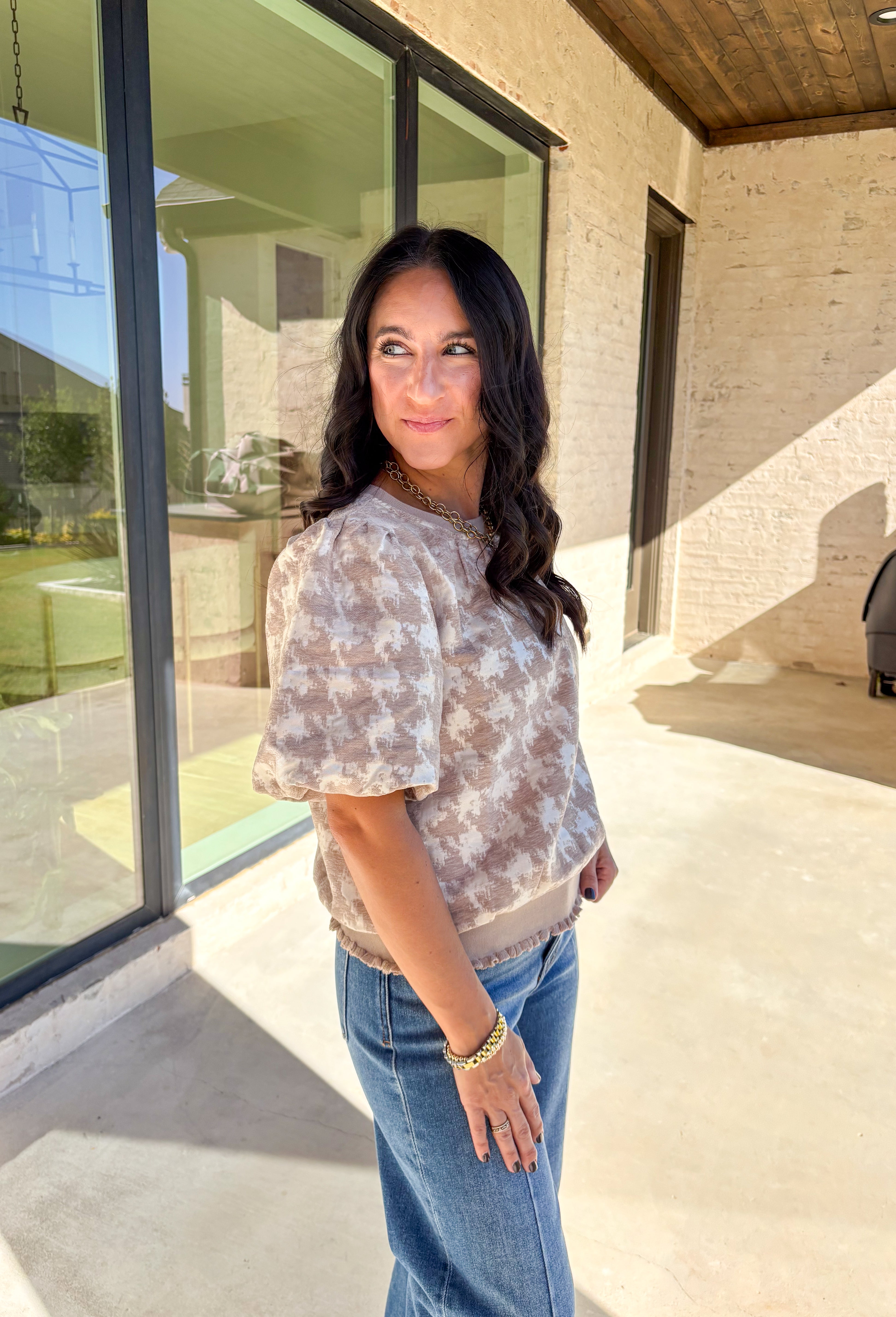 This taupe short sleeve top by Voy gives a modern twist to a timeless print. Designed with a textured abstract houndstooth pattern, it’s the perfect mix of classic and contemporary. The puff sleeves add a soft, feminine touch, while the lettuce hem brings a subtle edge to the silhouette. Lightweight and comfortable, this top easily transitions from weekday wear to special occasions.