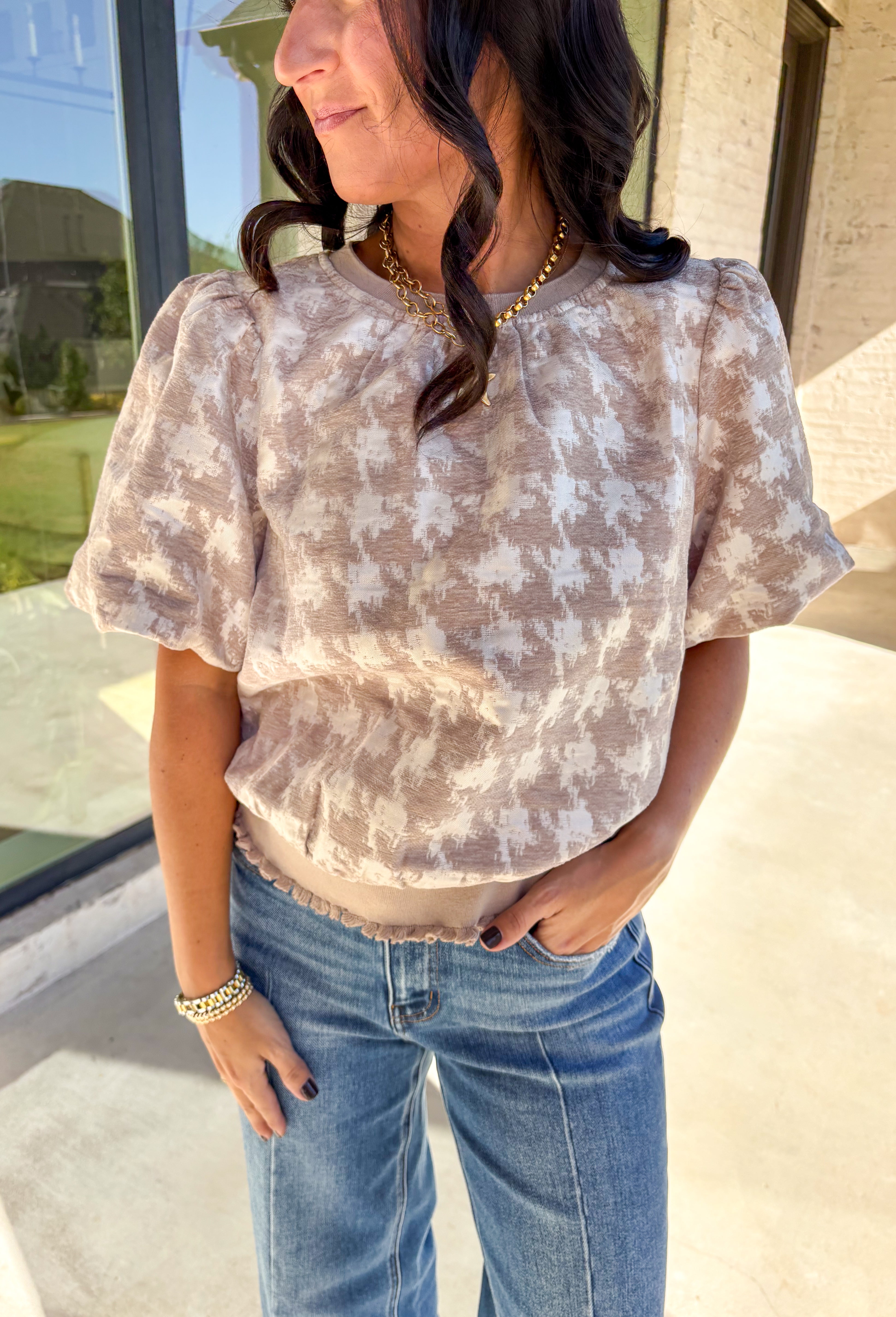 This taupe short sleeve top by Voy gives a modern twist to a timeless print. Designed with a textured abstract houndstooth pattern, it’s the perfect mix of classic and contemporary. The puff sleeves add a soft, feminine touch, while the lettuce hem brings a subtle edge to the silhouette. Lightweight and comfortable, this top easily transitions from weekday wear to special occasions.