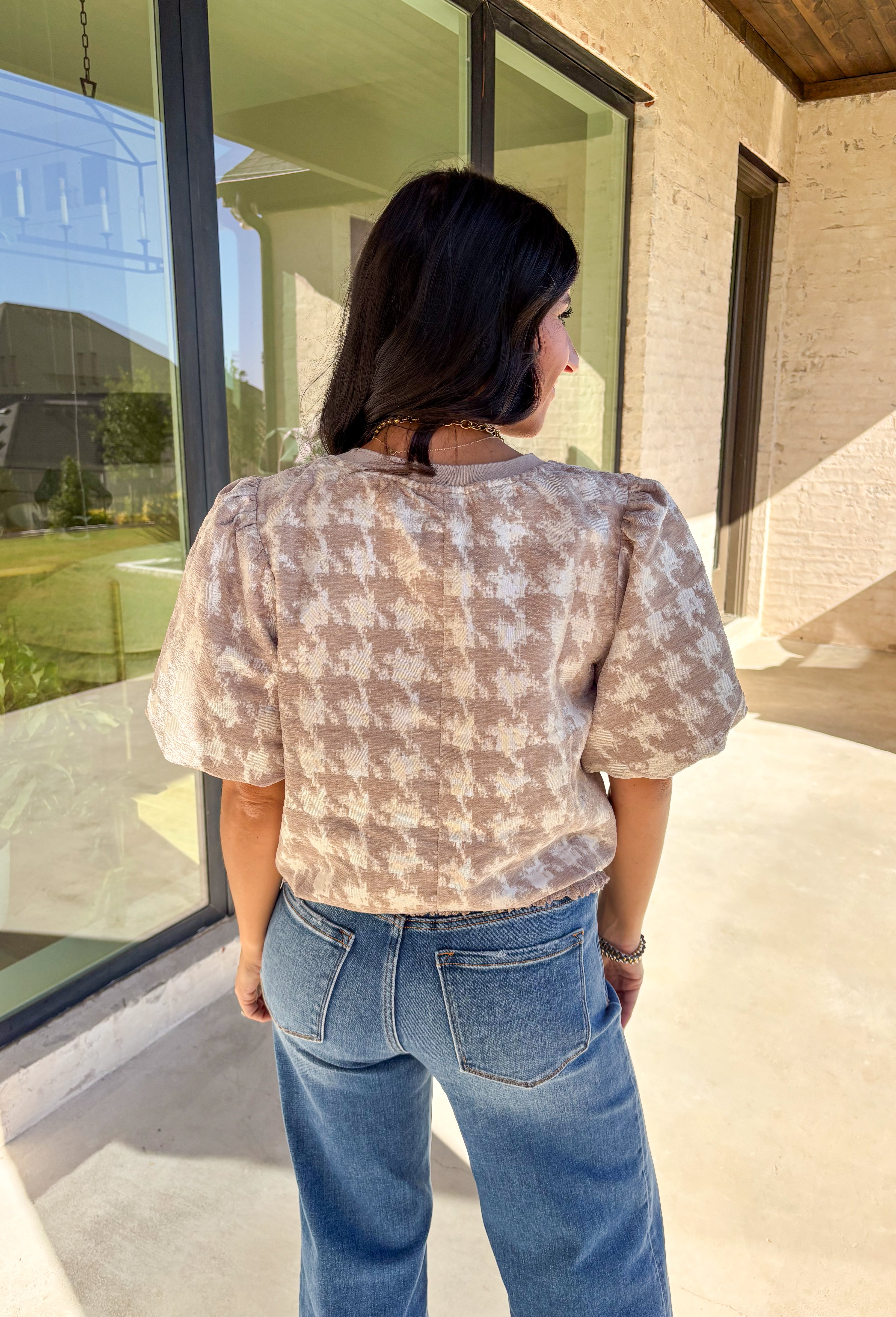 This taupe short sleeve top by Voy gives a modern twist to a timeless print. Designed with a textured abstract houndstooth pattern, it’s the perfect mix of classic and contemporary. The puff sleeves add a soft, feminine touch, while the lettuce hem brings a subtle edge to the silhouette. Lightweight and comfortable, this top easily transitions from weekday wear to special occasions.