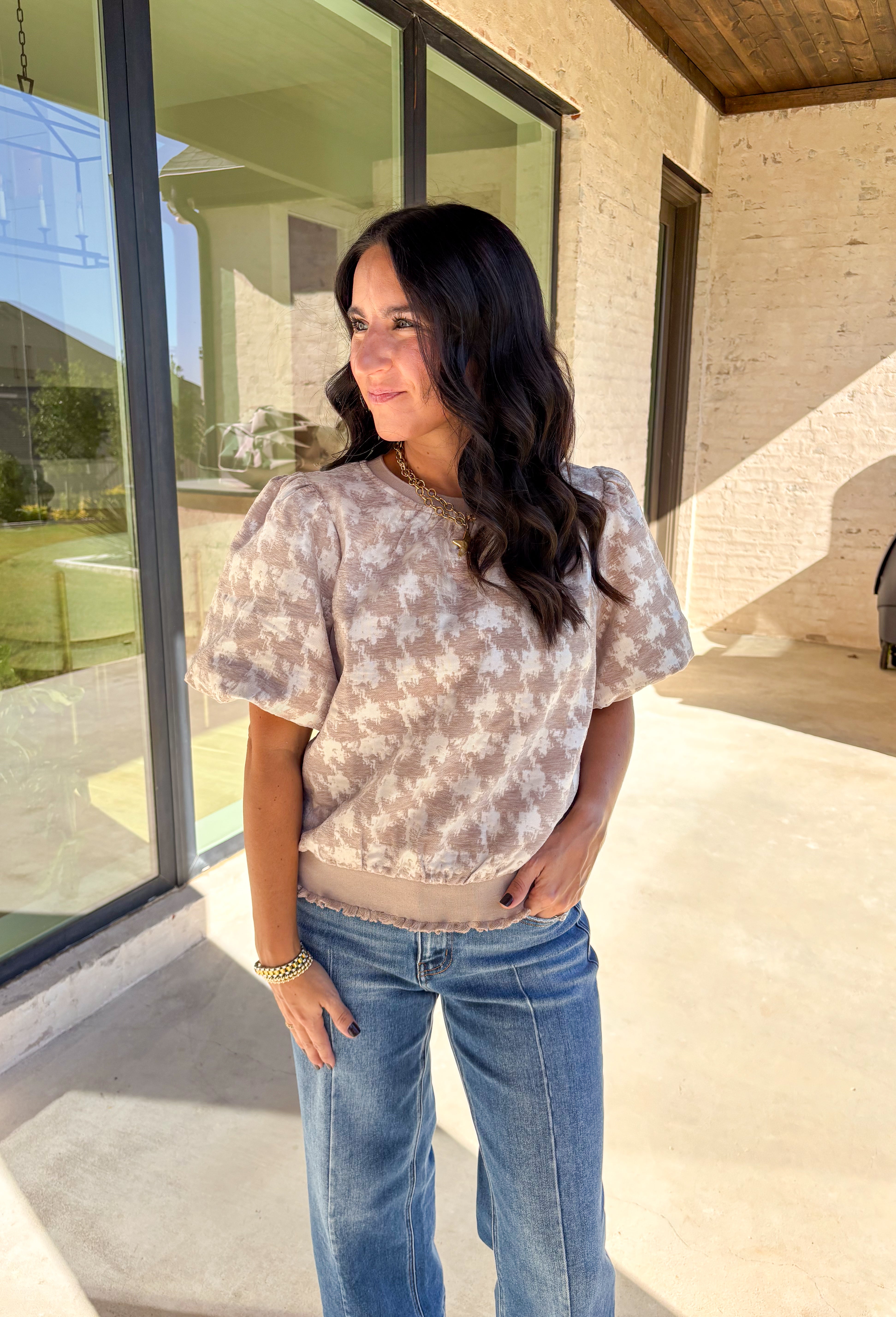 This taupe short sleeve top by Voy gives a modern twist to a timeless print. Designed with a textured abstract houndstooth pattern, it’s the perfect mix of classic and contemporary. The puff sleeves add a soft, feminine touch, while the lettuce hem brings a subtle edge to the silhouette. Lightweight and comfortable, this top easily transitions from weekday wear to special occasions.