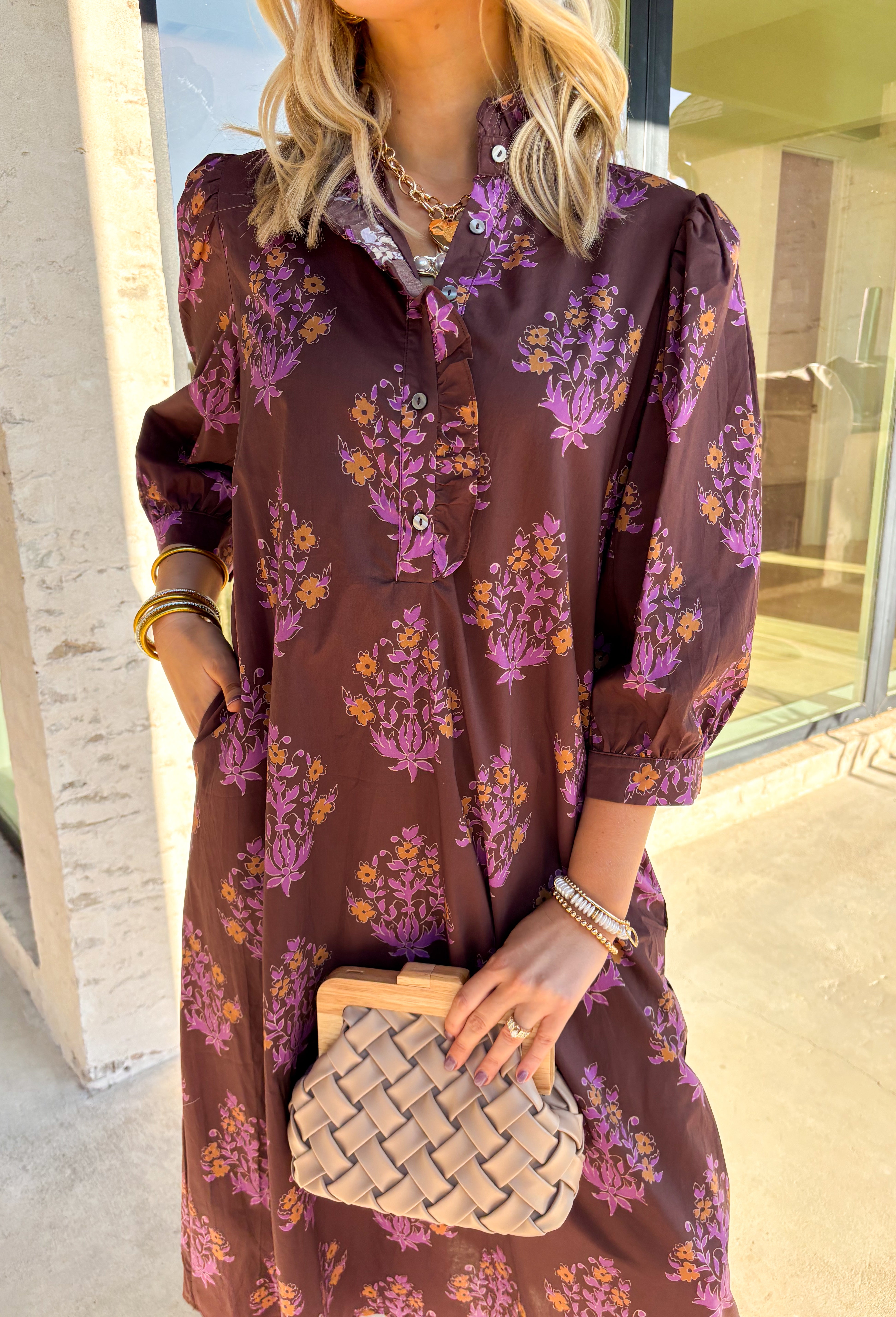 Earthy tones meet feminine charm in this beautiful botanical print midi dress by Entro. Designed with ¾ sleeves and a soft ruffle trim along the collar and front placket, it’s full of subtle details that make it feel special. The button-front design and side pockets bring functionality, while the brown base with purple and dark yellow florals gives it that perfect fall color palette. Fully lined and made from breathable cotton, it’s comfortable enough for all-day wear while keeping your look effortlessly po