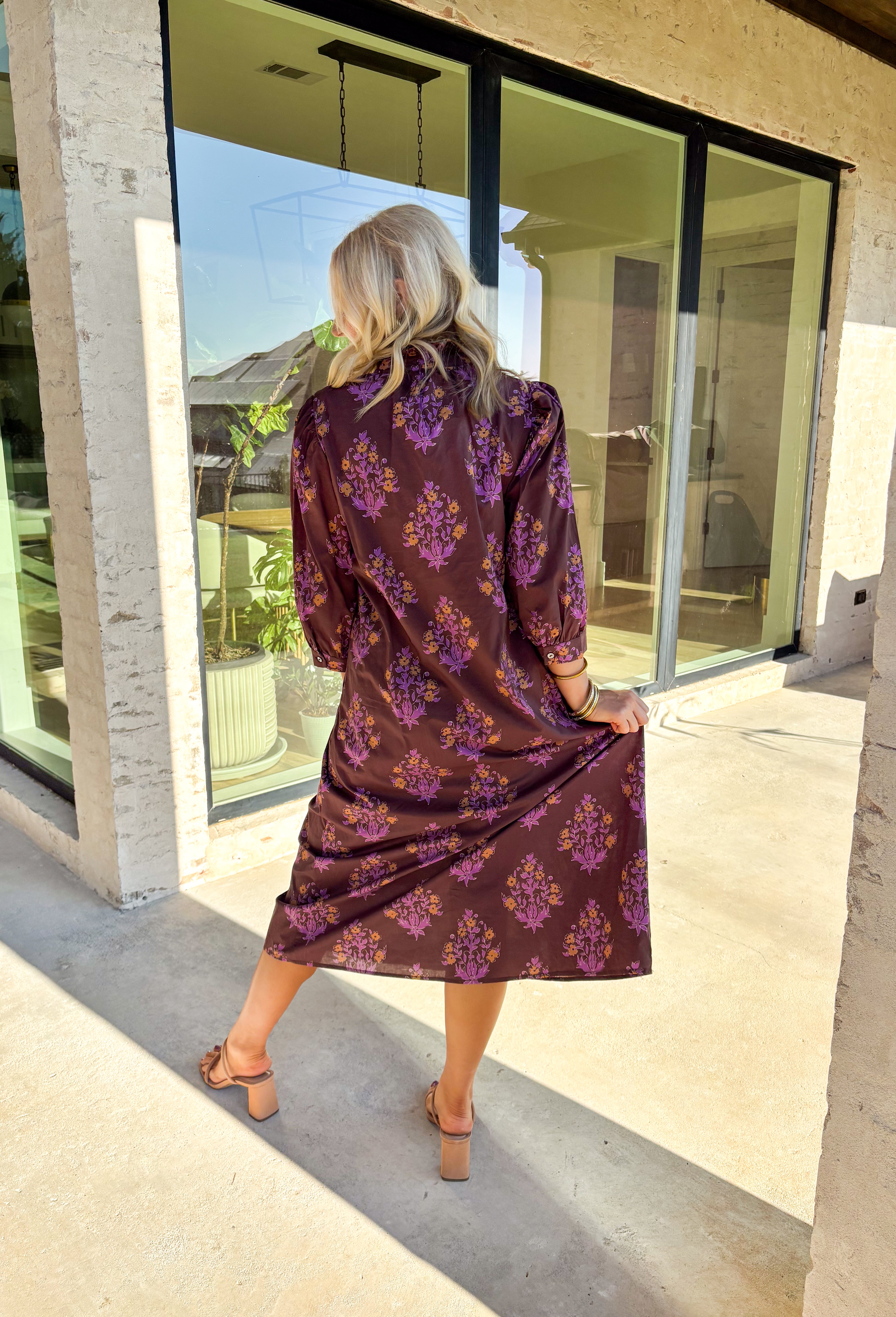 Earthy tones meet feminine charm in this beautiful botanical print midi dress by Entro. Designed with ¾ sleeves and a soft ruffle trim along the collar and front placket, it’s full of subtle details that make it feel special. The button-front design and side pockets bring functionality, while the brown base with purple and dark yellow florals gives it that perfect fall color palette. Fully lined and made from breathable cotton, it’s comfortable enough for all-day wear while keeping your look effortlessly po