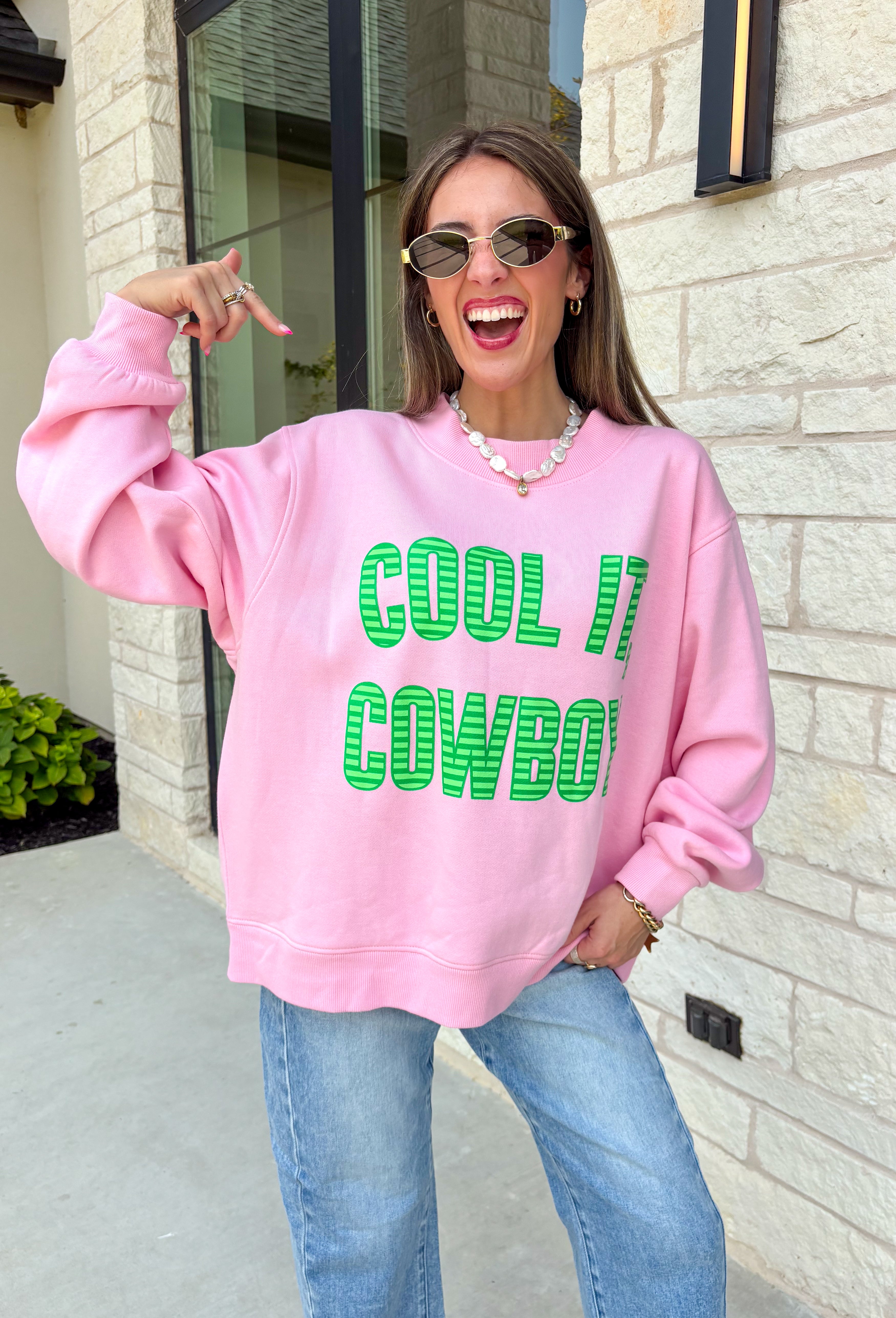 Add a little western attitude to your cozy season! This playful pink mock neck sweatshirt features a bold "Cool It, Cowboy" graphic in textured green striped lettering for the perfect mix of retro charm and everyday comfort. The ribbed neckline, cuffs, and hem give this fleece-lined pullover an elevated finish, making it a standout piece you'll love wearing on crisp fall days.