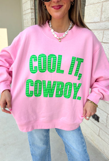 Add a little western attitude to your cozy season! This playful pink mock neck sweatshirt features a bold "Cool It, Cowboy" graphic in textured green striped lettering for the perfect mix of retro charm and everyday comfort. The ribbed neckline, cuffs, and hem give this fleece-lined pullover an elevated finish, making it a standout piece you'll love wearing on crisp fall days.