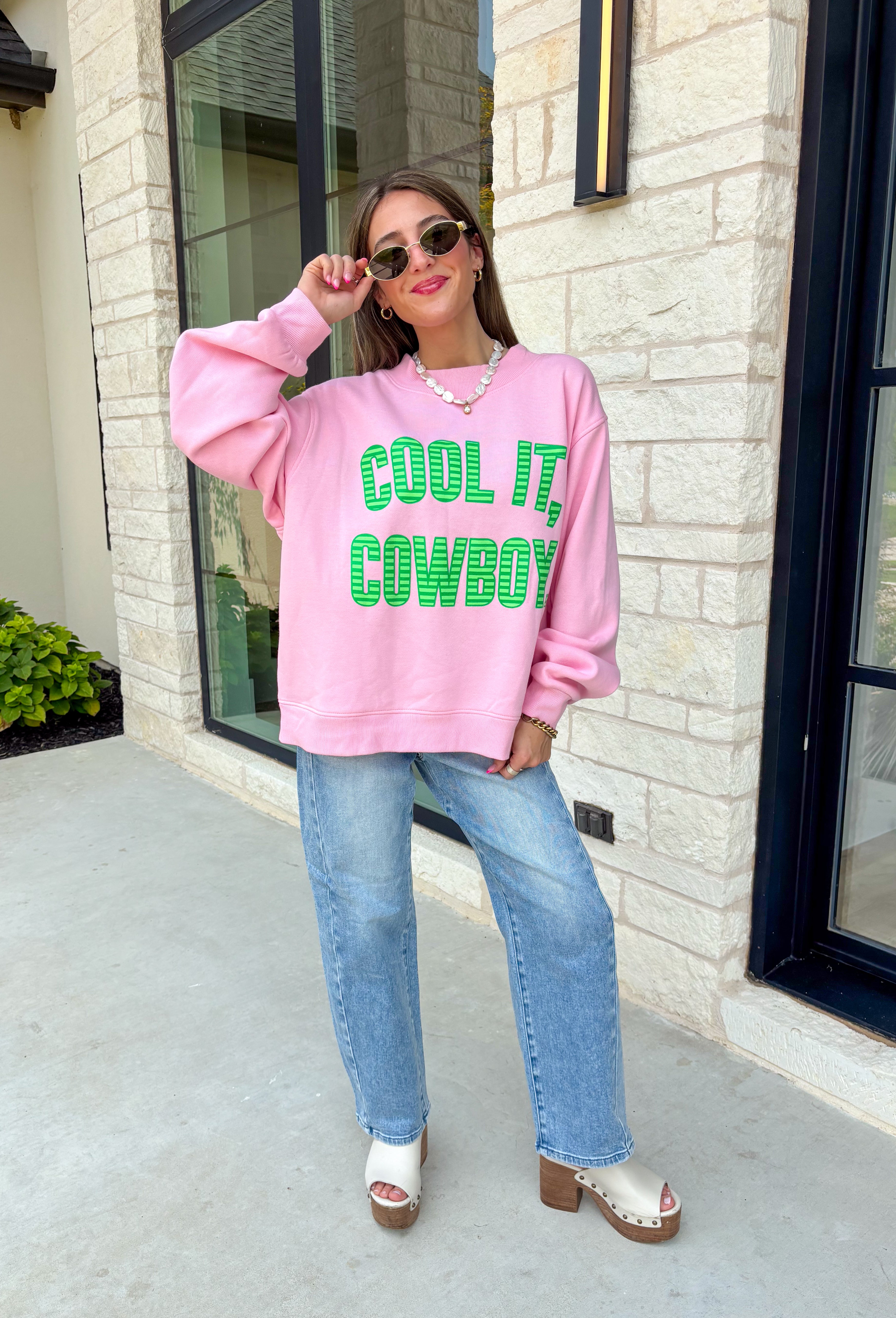 Add a little western attitude to your cozy season! This playful pink mock neck sweatshirt features a bold "Cool It, Cowboy" graphic in textured green striped lettering for the perfect mix of retro charm and everyday comfort. The ribbed neckline, cuffs, and hem give this fleece-lined pullover an elevated finish, making it a standout piece you'll love wearing on crisp fall days.