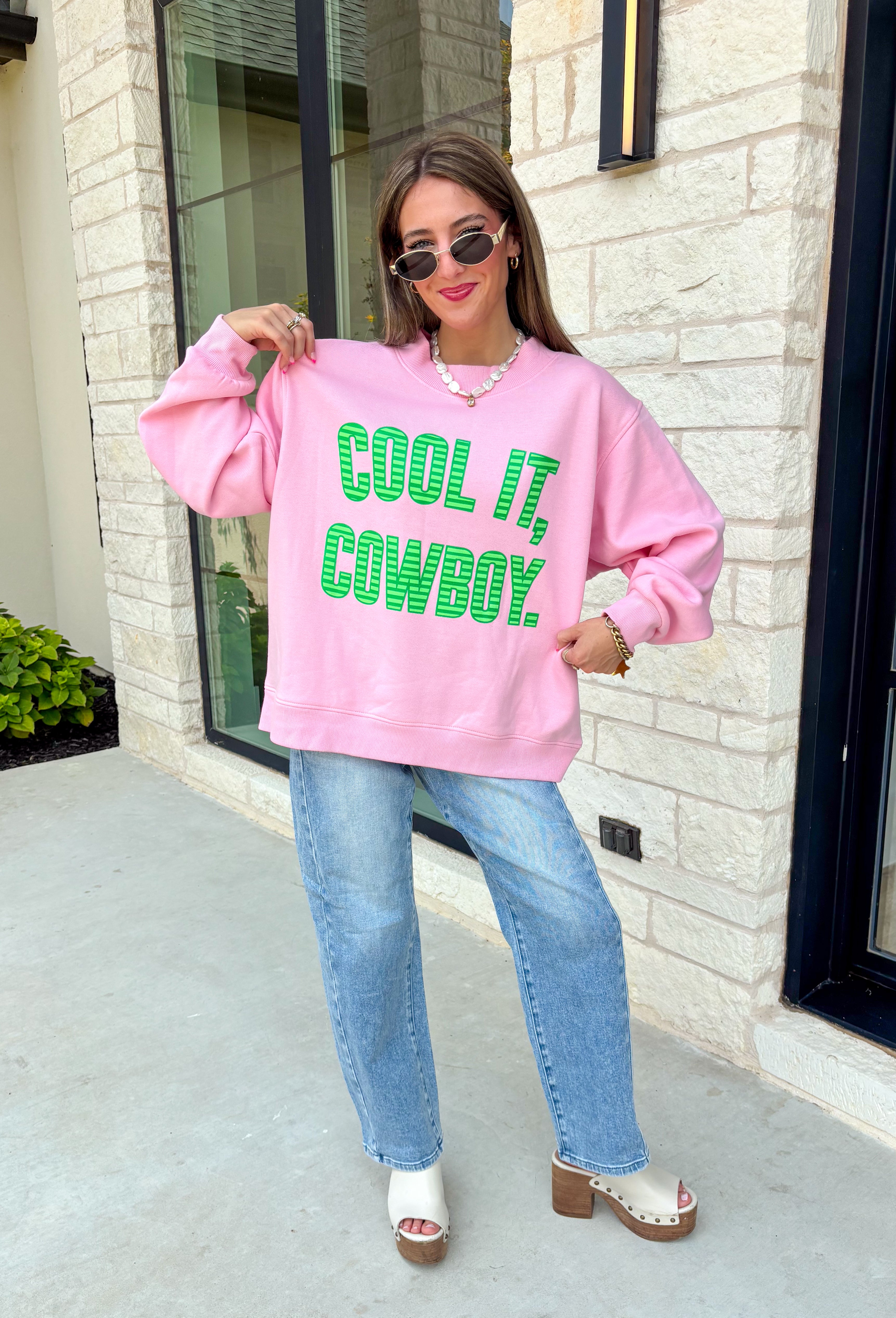 Add a little western attitude to your cozy season! This playful pink mock neck sweatshirt features a bold "Cool It, Cowboy" graphic in textured green striped lettering for the perfect mix of retro charm and everyday comfort. The ribbed neckline, cuffs, and hem give this fleece-lined pullover an elevated finish, making it a standout piece you'll love wearing on crisp fall days.