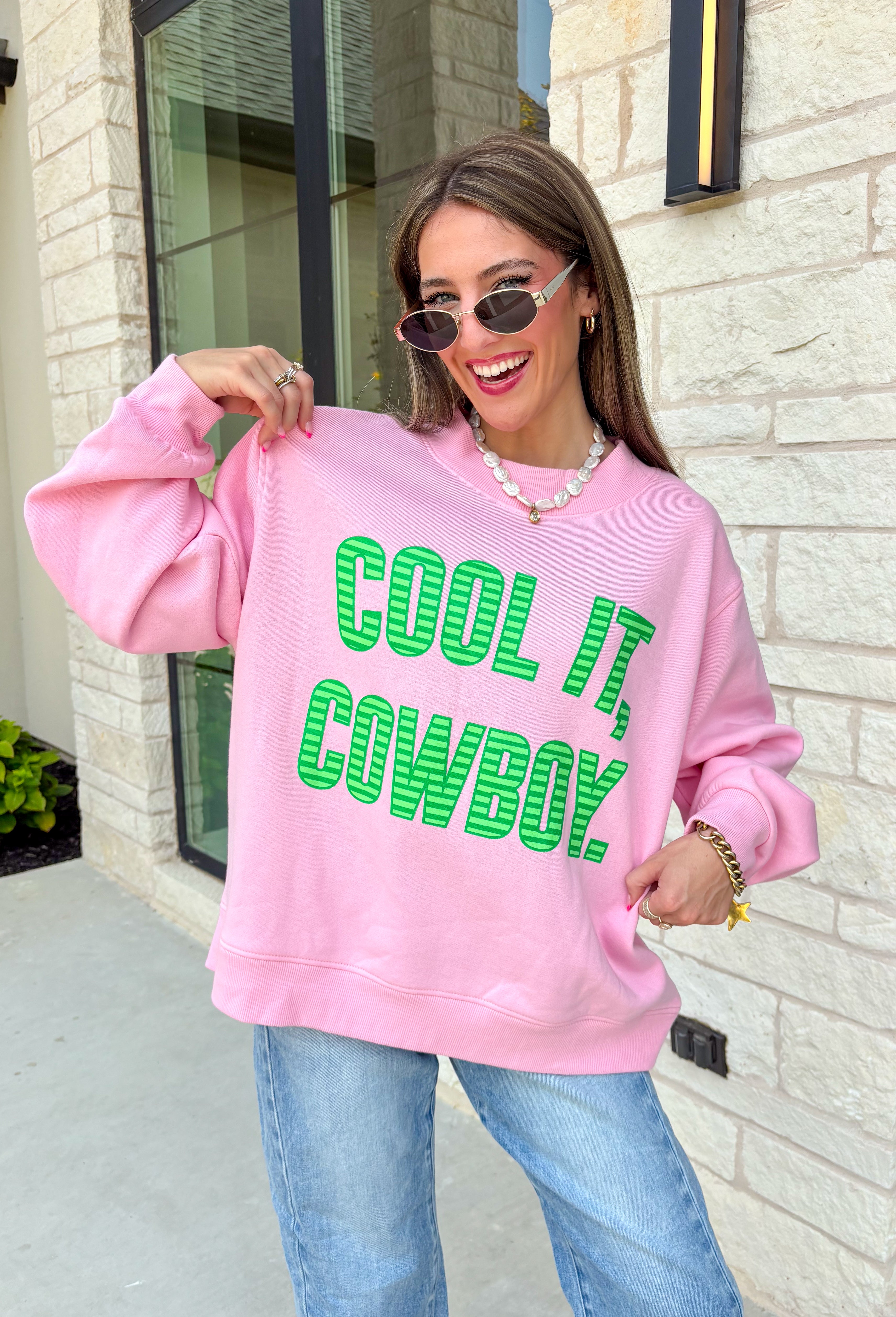 Add a little western attitude to your cozy season! This playful pink mock neck sweatshirt features a bold "Cool It, Cowboy" graphic in textured green striped lettering for the perfect mix of retro charm and everyday comfort. The ribbed neckline, cuffs, and hem give this fleece-lined pullover an elevated finish, making it a standout piece you'll love wearing on crisp fall days.
