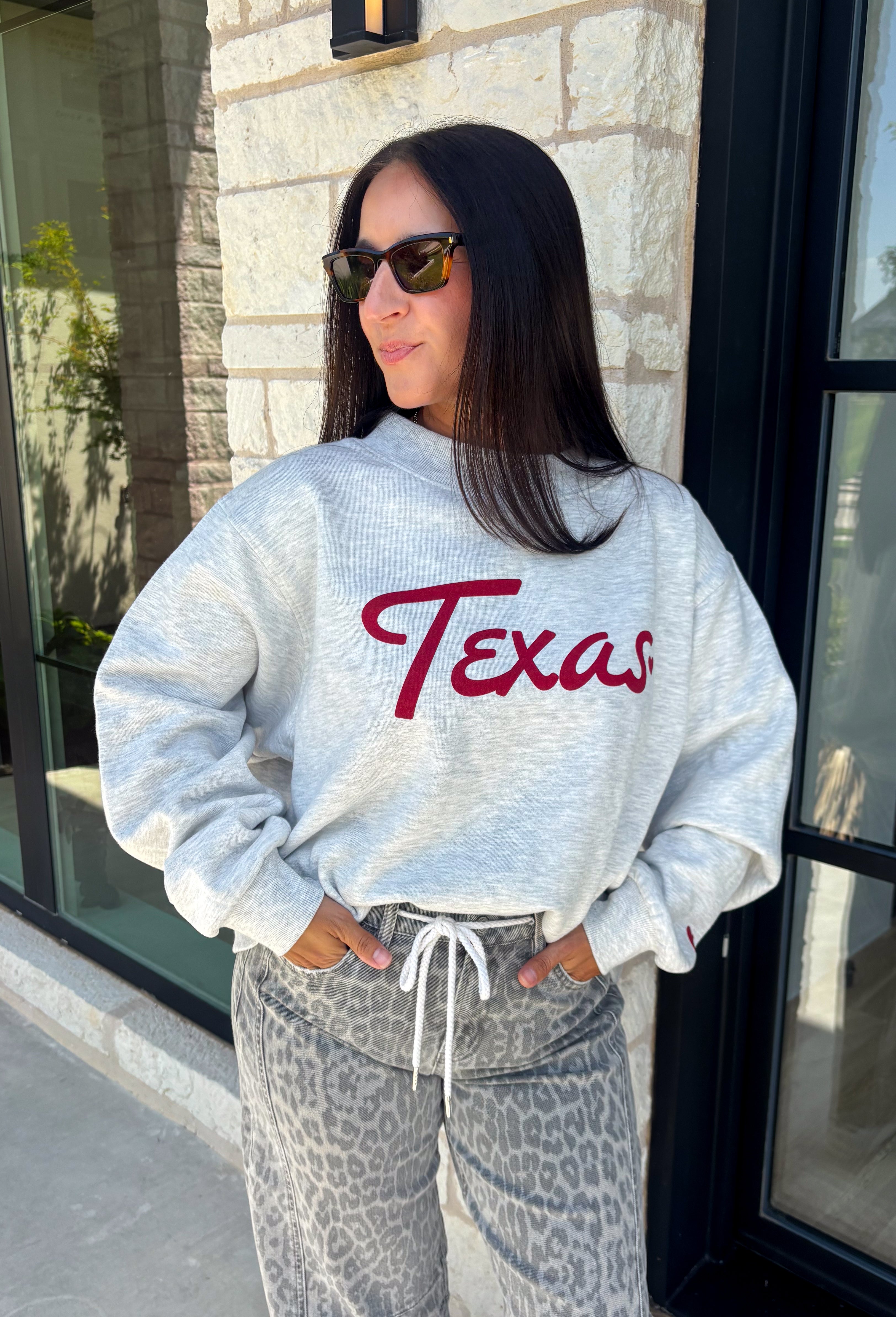Show your Texas pride in the coziest way possible! This ash grey mock neck sweatshirt blends everyday comfort with timeless style, featuring "Texas" in soft script across the chest and a sweet heart detail on the sleeve. The fleece-lined interior keeps you warm and cozy, while the classic silhouette makes it an easy favorite for everything from football Saturdays and coffee runs to relaxed weekends at home. 