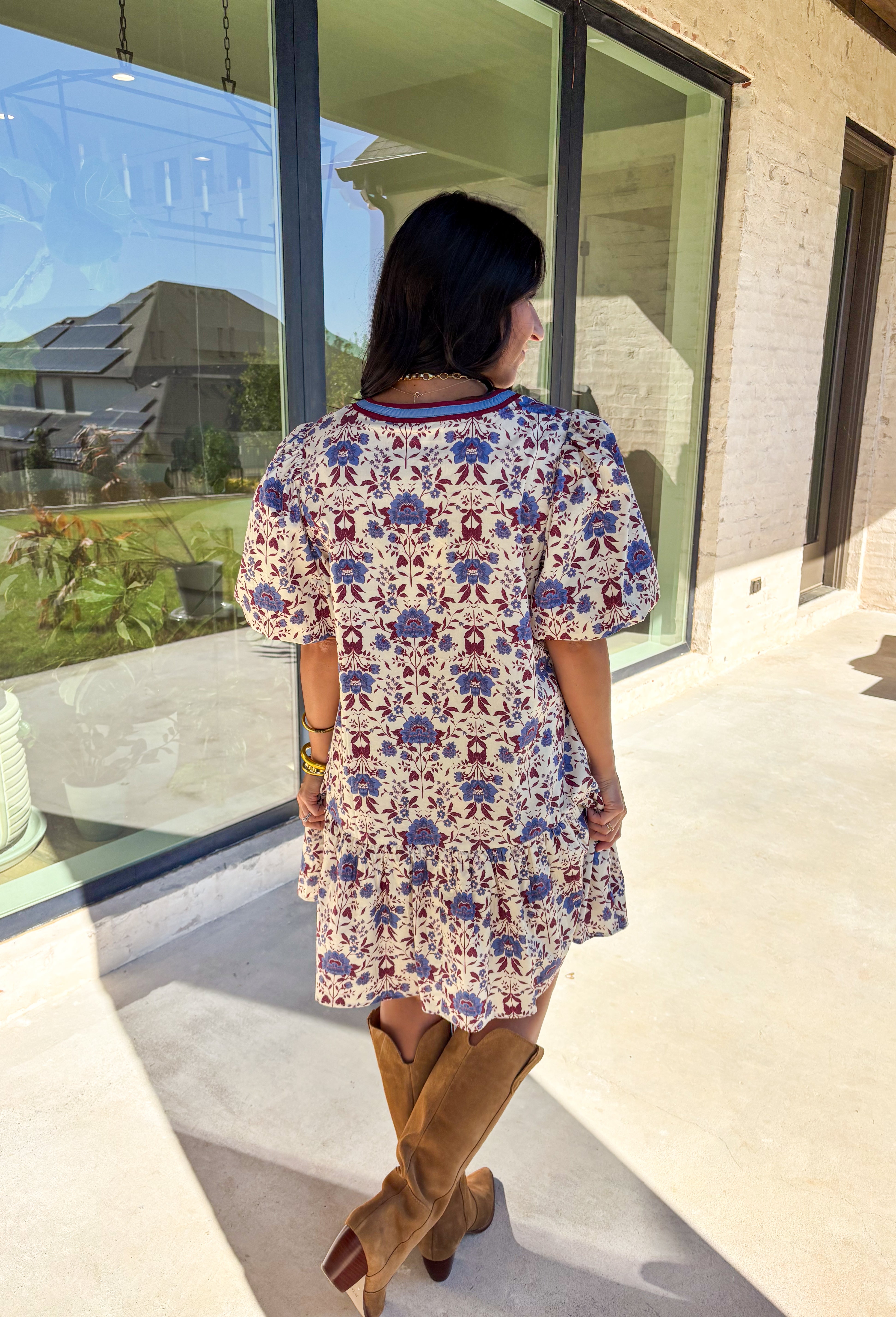 Romantic florals meet cozy charm in this cream short sleeve dress. Designed with shades of burgundy and blue for an autumn-inspired palette, it features a botanical print and contrast binding along the v-neckline for a polished finish. The puff sleeves add a playful touch, while the ruffle hem brings soft movement. Fully lined with side pockets for practicality, this dress is as easy to wear as it is beautiful.