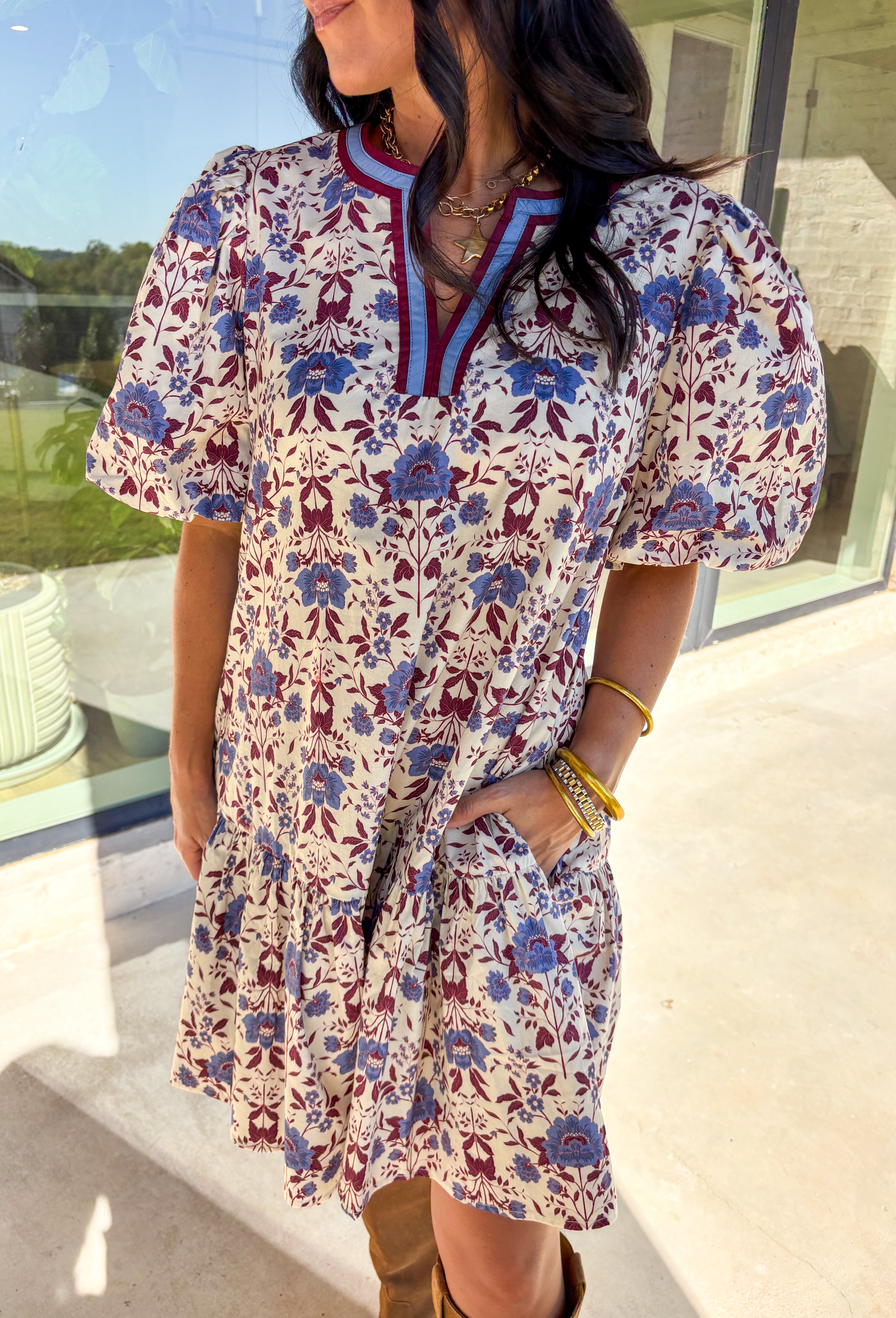 Romantic florals meet cozy charm in this cream short sleeve dress. Designed with shades of burgundy and blue for an autumn-inspired palette, it features a botanical print and contrast binding along the v-neckline for a polished finish. The puff sleeves add a playful touch, while the ruffle hem brings soft movement. Fully lined with side pockets for practicality, this dress is as easy to wear as it is beautiful.