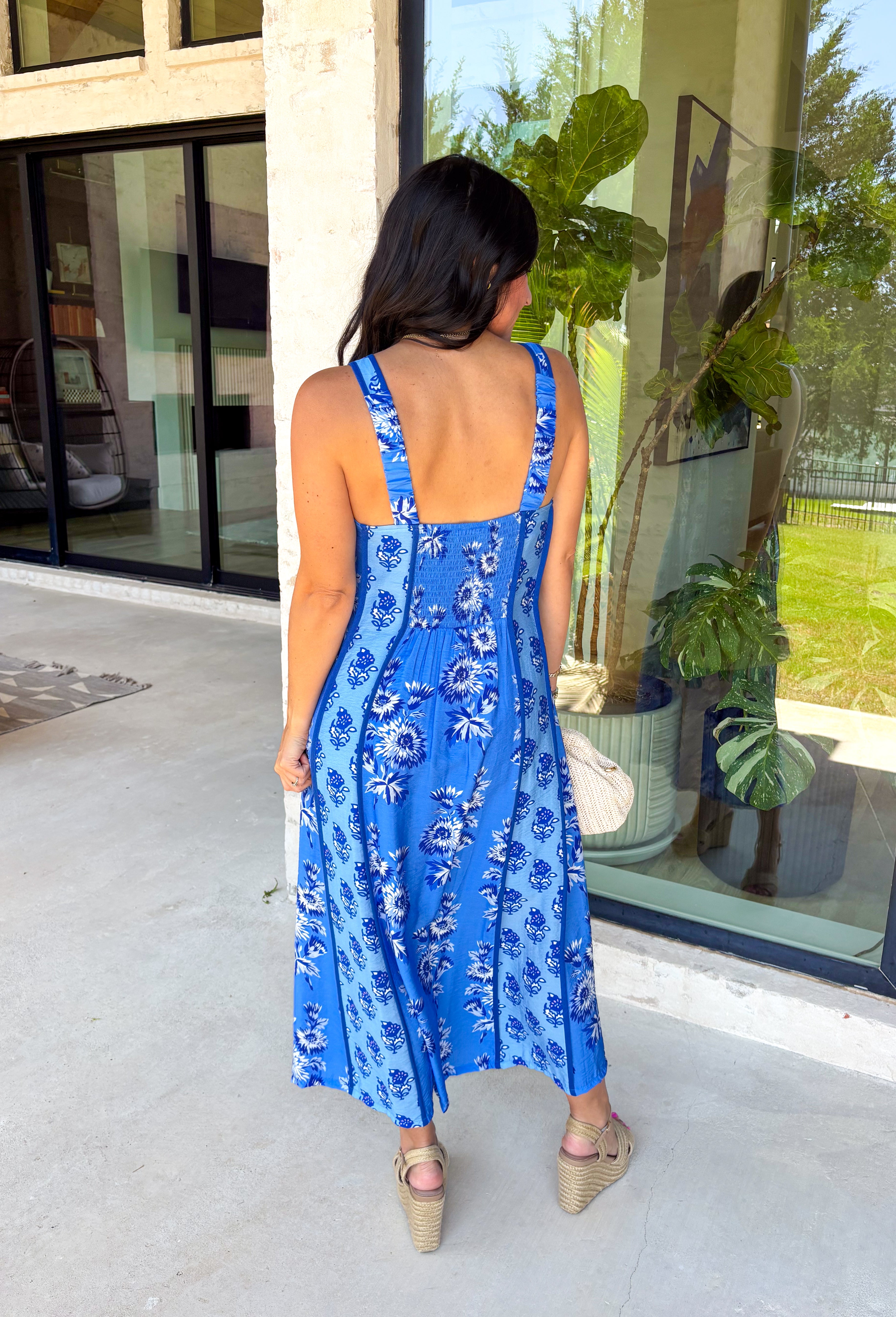 Feminine, fresh, and perfect for sunny days! This sleeveless blue midi dress features a beautiful floral print that feels soft and romantic. Darker blue trim paneling throughout adds a lovely contrast that highlights the silhouette and gives the dress a little extra detail. Smocking along the back and on the back straps creates a comfortable, flexible fit while keeping the shape flattering. 