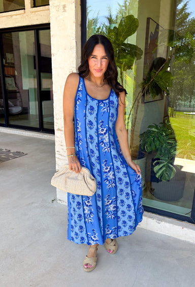 Feminine, fresh, and perfect for sunny days! This sleeveless blue midi dress features a beautiful floral print that feels soft and romantic. Darker blue trim paneling throughout adds a lovely contrast that highlights the silhouette and gives the dress a little extra detail. Smocking along the back and on the back straps creates a comfortable, flexible fit while keeping the shape flattering. 