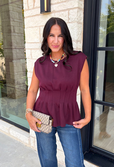 Rich seasonal color meets effortless style in this beautiful burgundy sleeveless top. Designed with flattering pleated waist detailing, this timeless piece creates a polished silhouette that's easy to dress up or down. The soft knit fabric offers all-day comfort, making it perfect for layering under blazers and jackets throughout the fall or wearing on its own during warmer autumn afternoons. 