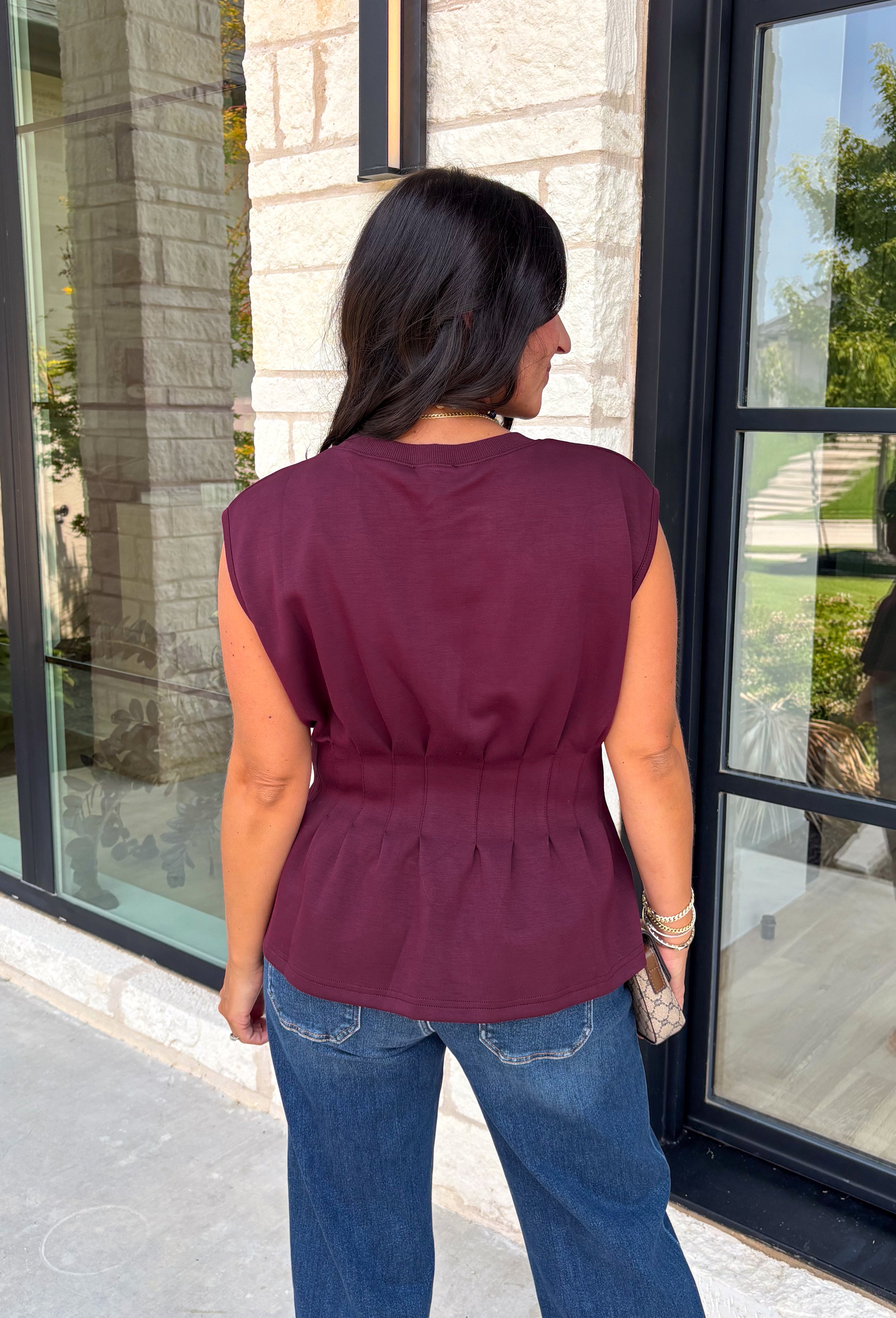Rich seasonal color meets effortless style in this beautiful burgundy sleeveless top. Designed with flattering pleated waist detailing, this timeless piece creates a polished silhouette that's easy to dress up or down. The soft knit fabric offers all-day comfort, making it perfect for layering under blazers and jackets throughout the fall or wearing on its own during warmer autumn afternoons. 