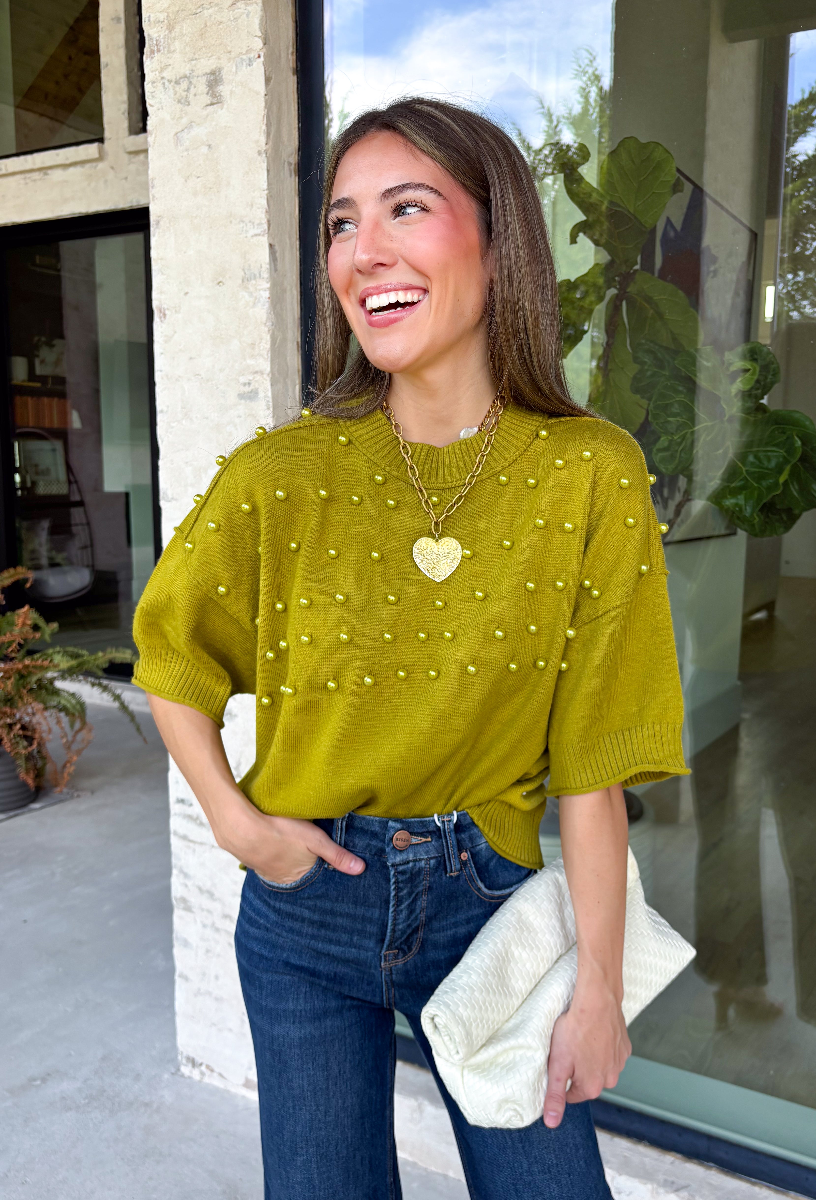 A rich olive green gets a pretty update with this pearl-detailed short sleeve sweater from Glam. Pearl detailing throughout adds a special touch to the soft knit, making it easy to dress up while still keeping that cozy, everyday feel. Exposed hems bring in a relaxed finish, while ribbed detailing along the neckline, sleeve cuffs, and hem gives it a classic sweater look. Wear it to the office, dinner plans, or anytime your outfit could use a little something extra.