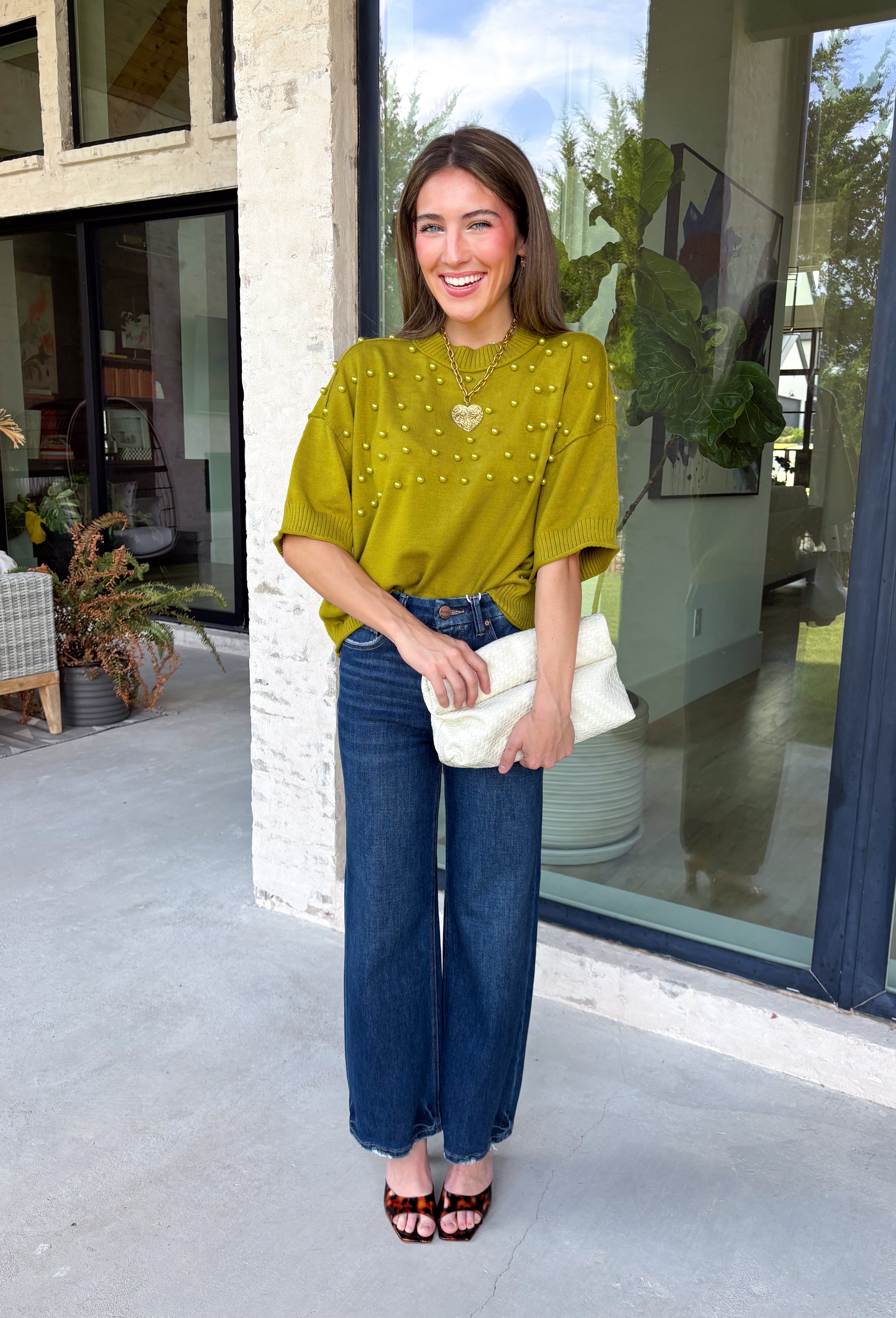 A rich olive green gets a pretty update with this pearl-detailed short sleeve sweater from Glam. Pearl detailing throughout adds a special touch to the soft knit, making it easy to dress up while still keeping that cozy, everyday feel. Exposed hems bring in a relaxed finish, while ribbed detailing along the neckline, sleeve cuffs, and hem gives it a classic sweater look. Wear it to the office, dinner plans, or anytime your outfit could use a little something extra.